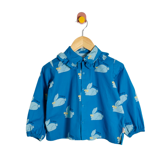 Blue children's top with animal prints on a wooden hanger against a white background