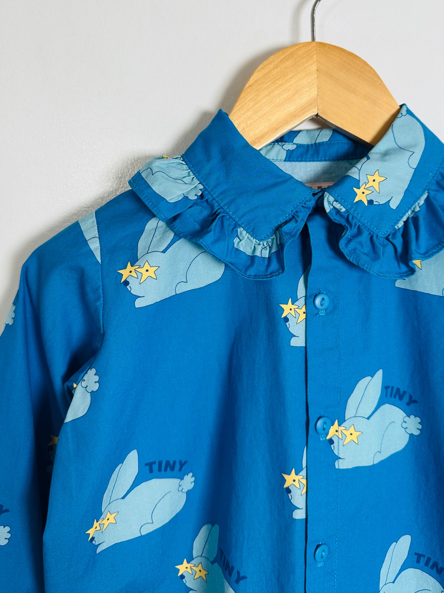 Blue children's shirt with bunny and star pattern on a wooden hanger against a white background