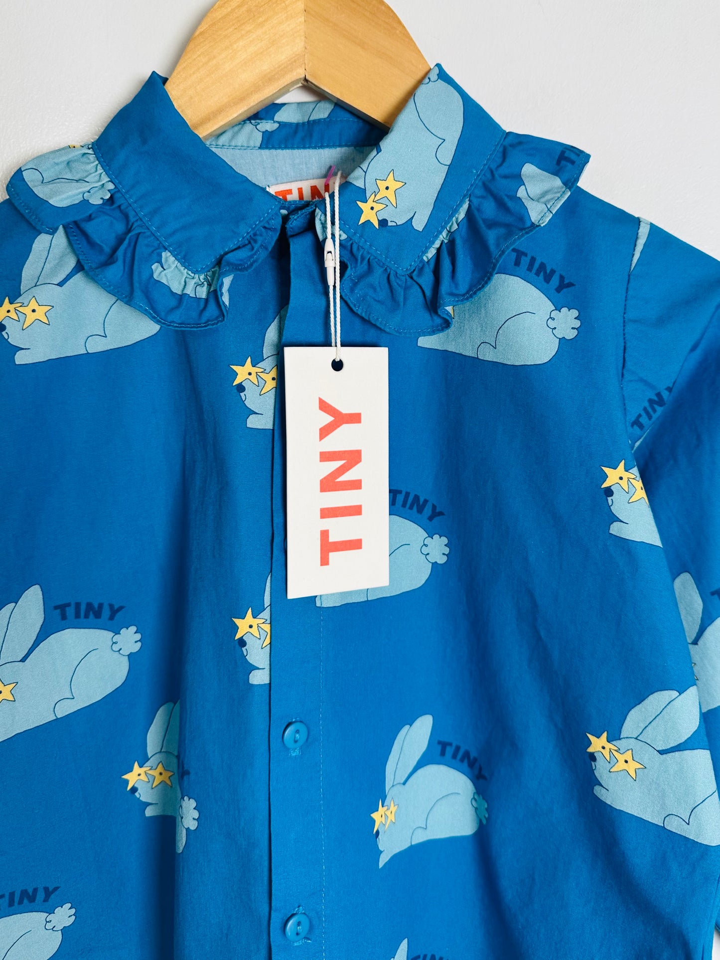 Blue children's top with animal pattern and 'TINY' tag on a hanger