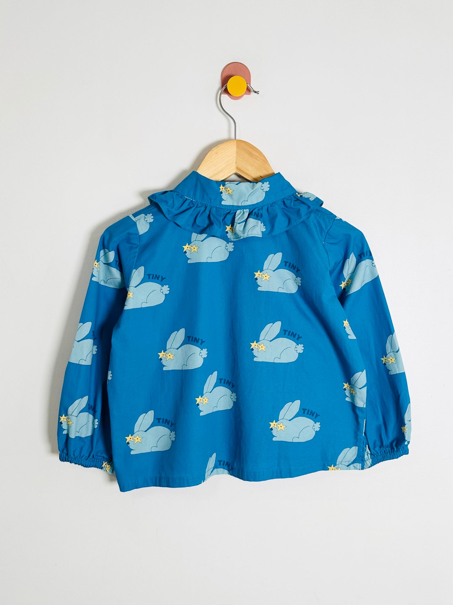 Blue children's blouse with bunny print on a hanger against a white background