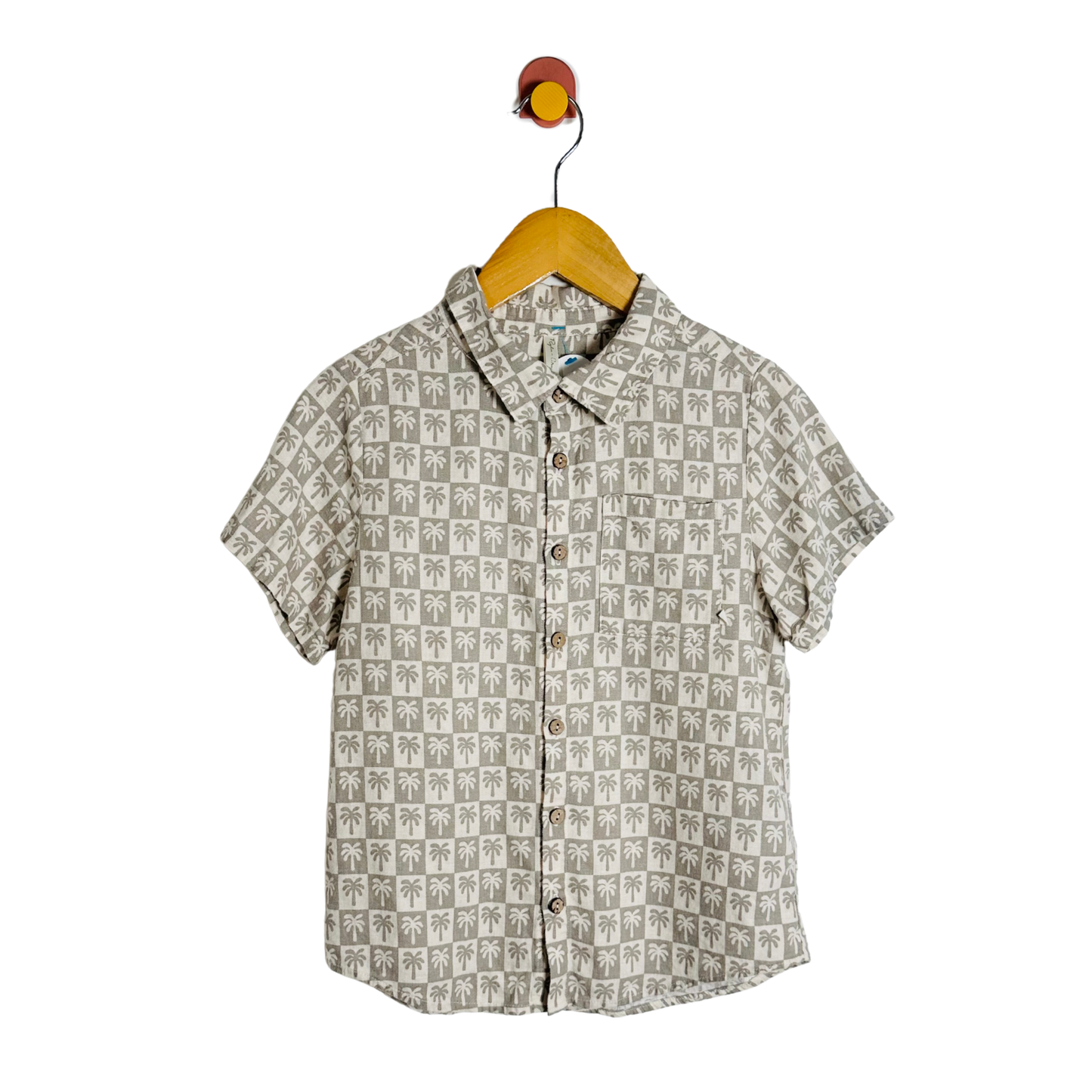 Short-sleeve shirt with palm tree pattern on a hanger against a white background