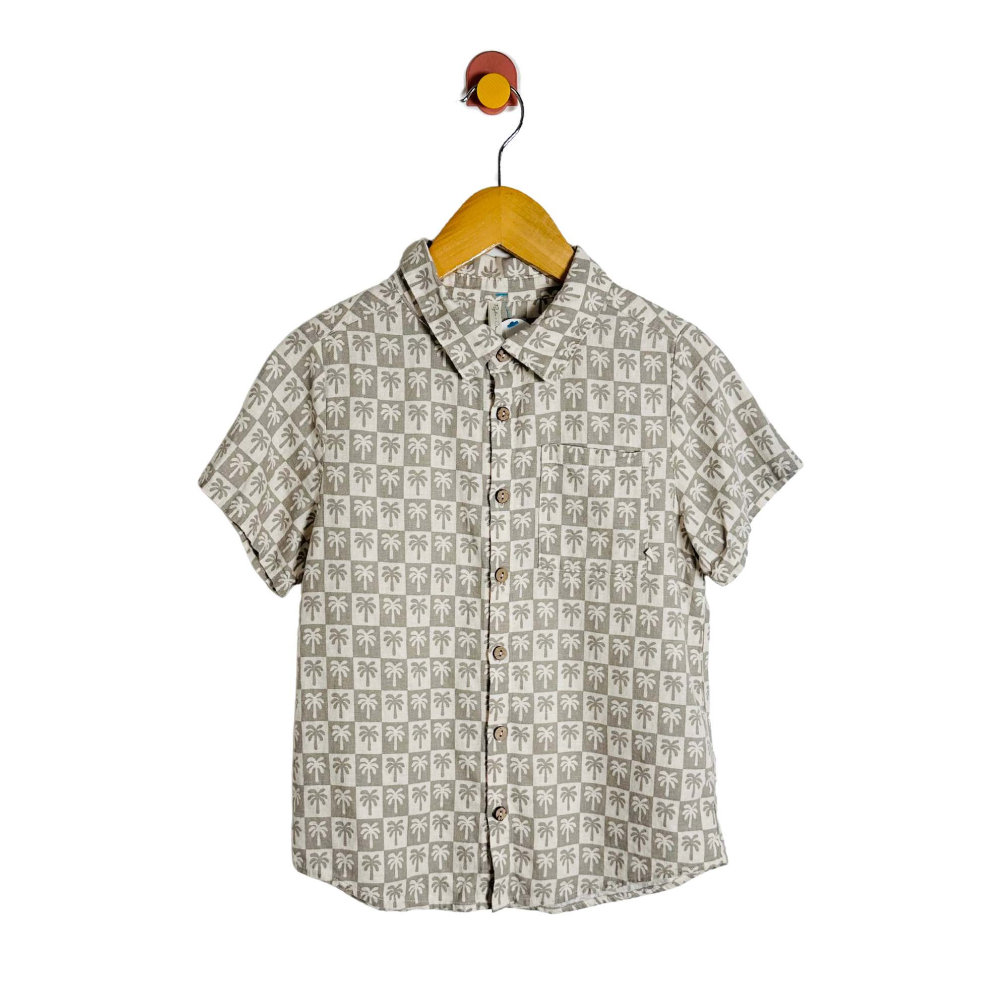 Short-sleeve shirt with palm tree pattern on a hanger against a white background