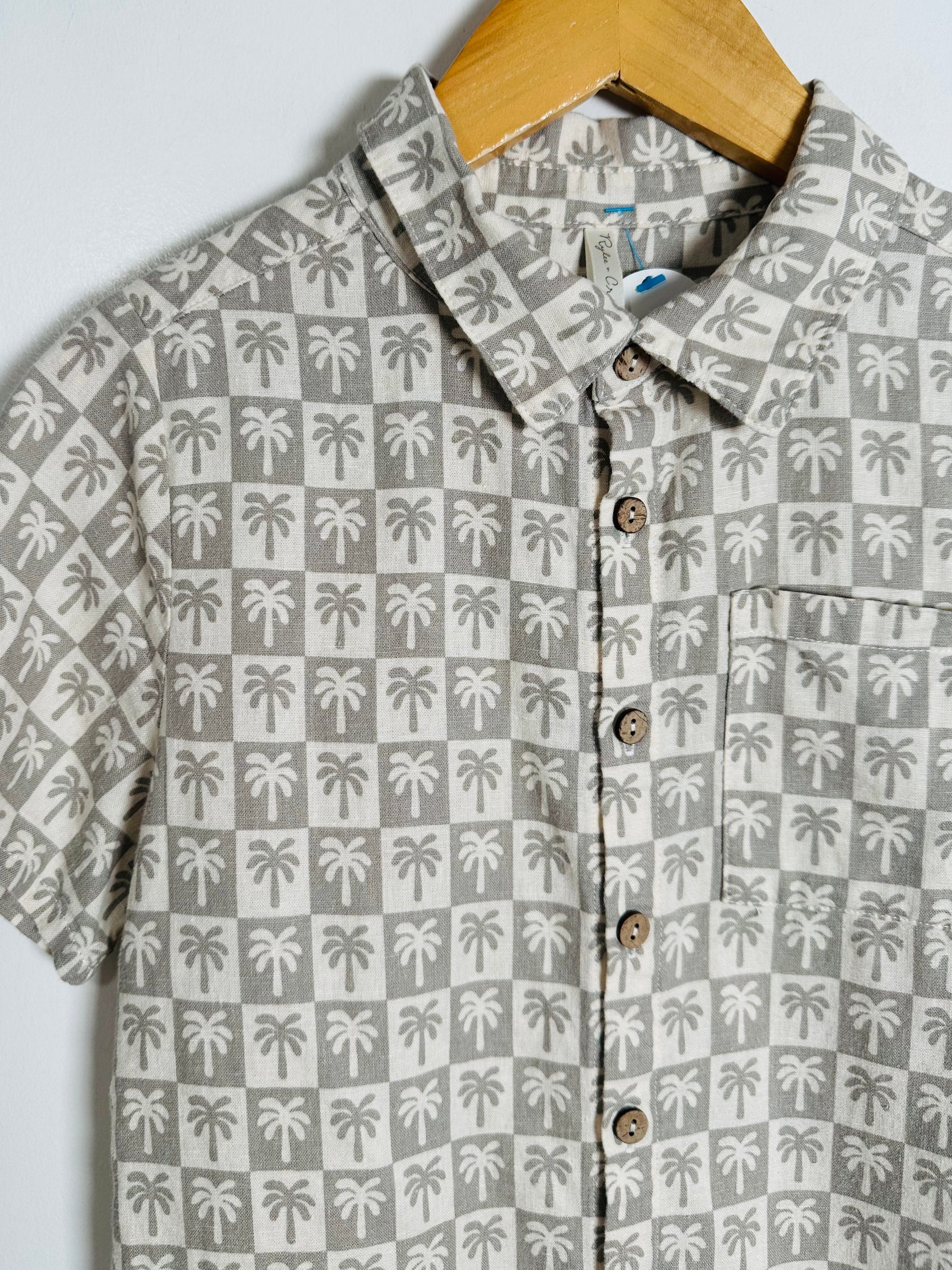 Button-up shirt with palm tree pattern on a hanger against a light background