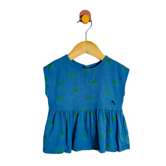 Blue top with green patterns on a wooden hanger against a white background