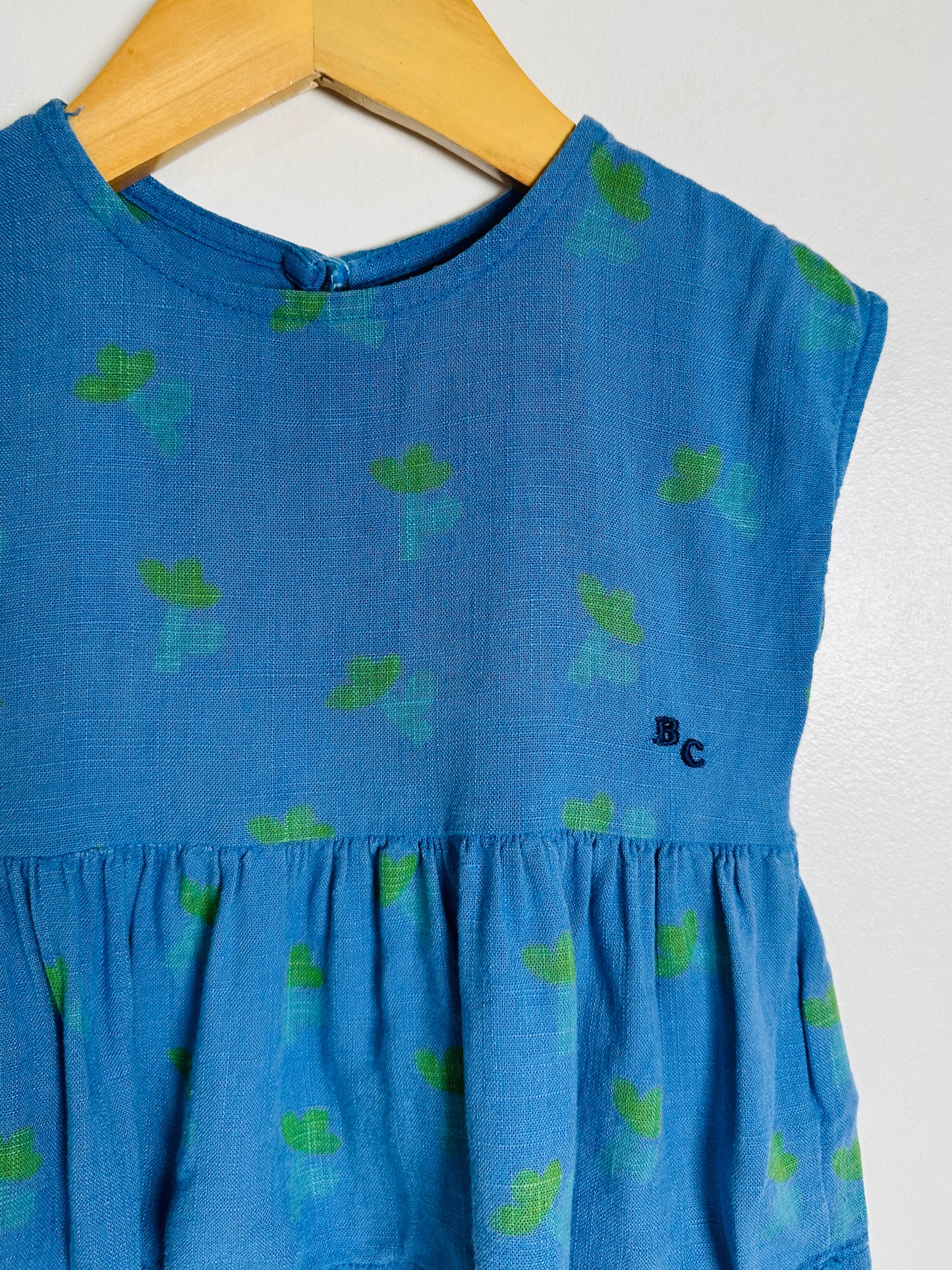 Blue top with green patterns on a wooden hanger against a white background