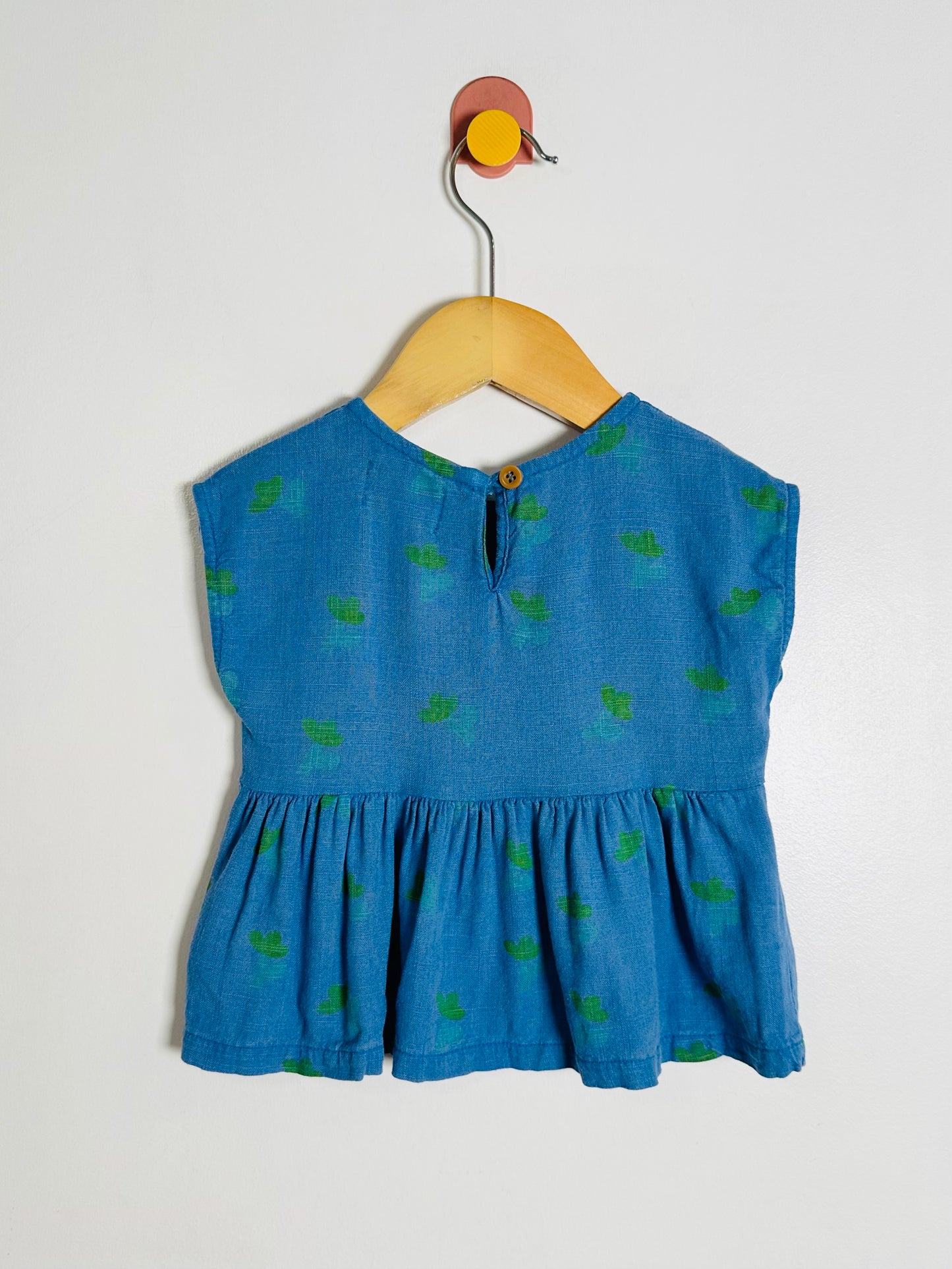 Blue children's top with green patterns on a hanger against a white background