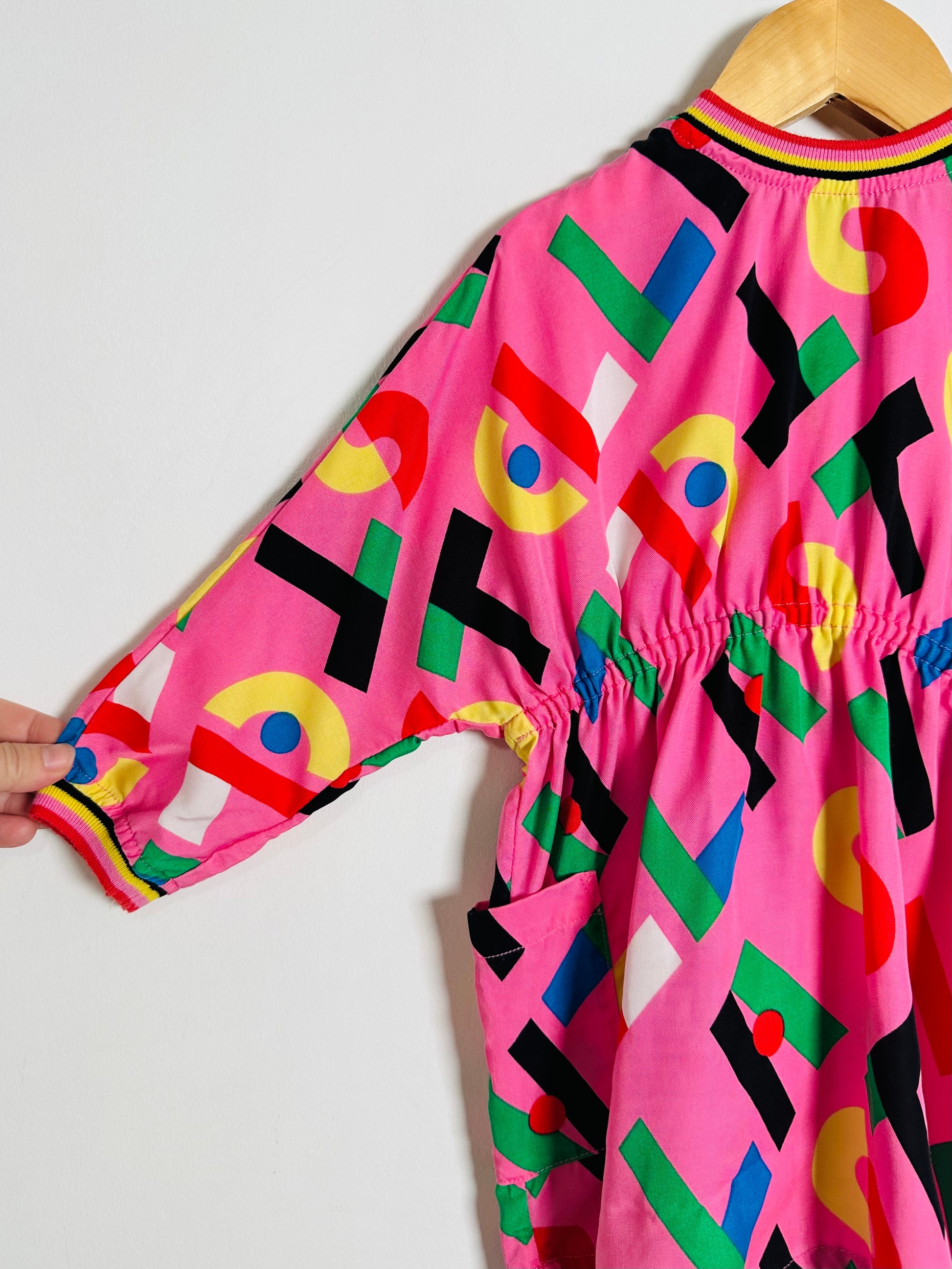 Colorful geometric-patterned pink outfit on a hanger against a white background
