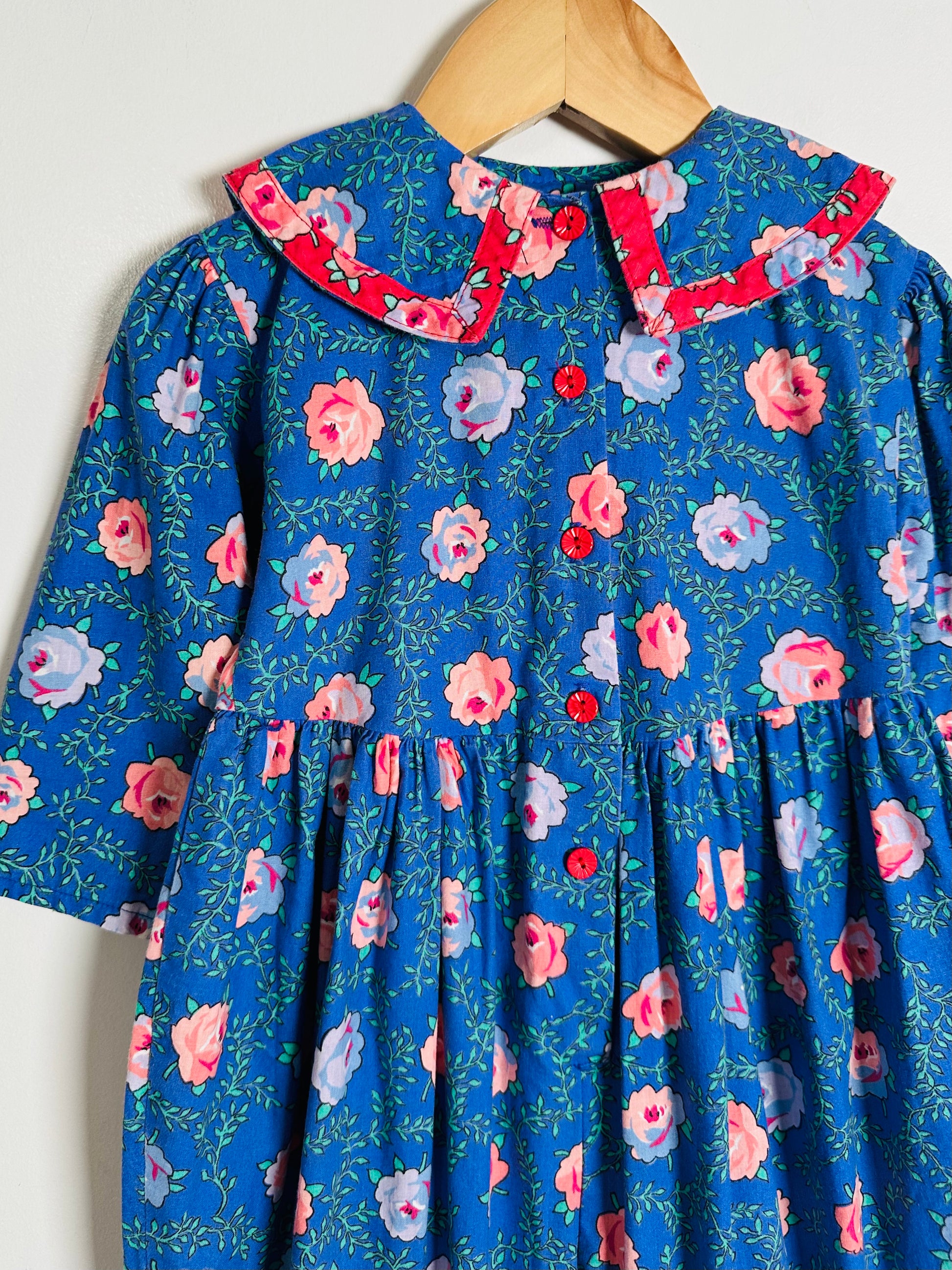 Blue floral romper with a red collar on a hanger against a white background