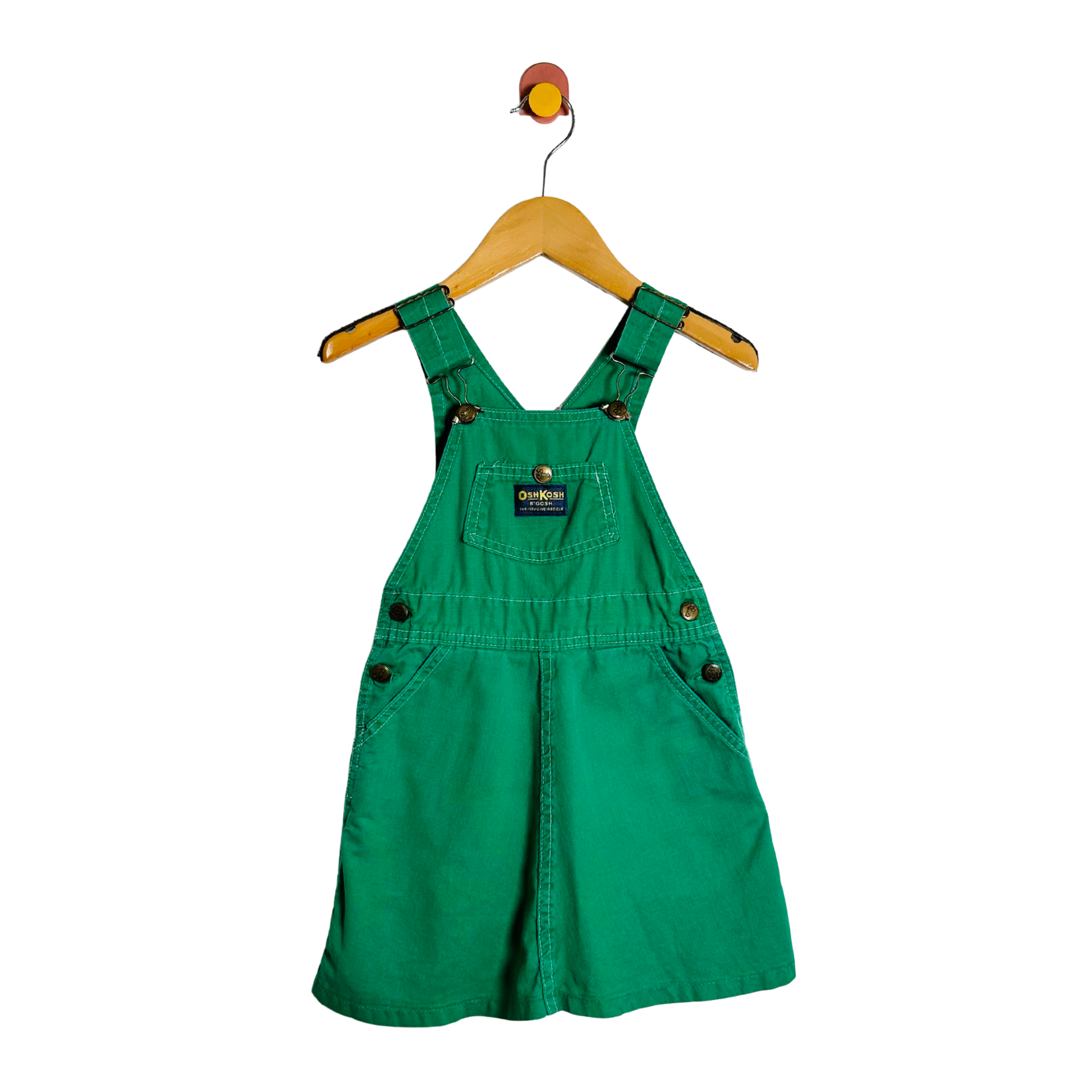 Green denim overall dress on a hanger against a white background