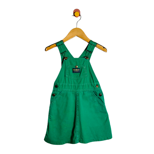 Green denim overall dress on a hanger against a white background
