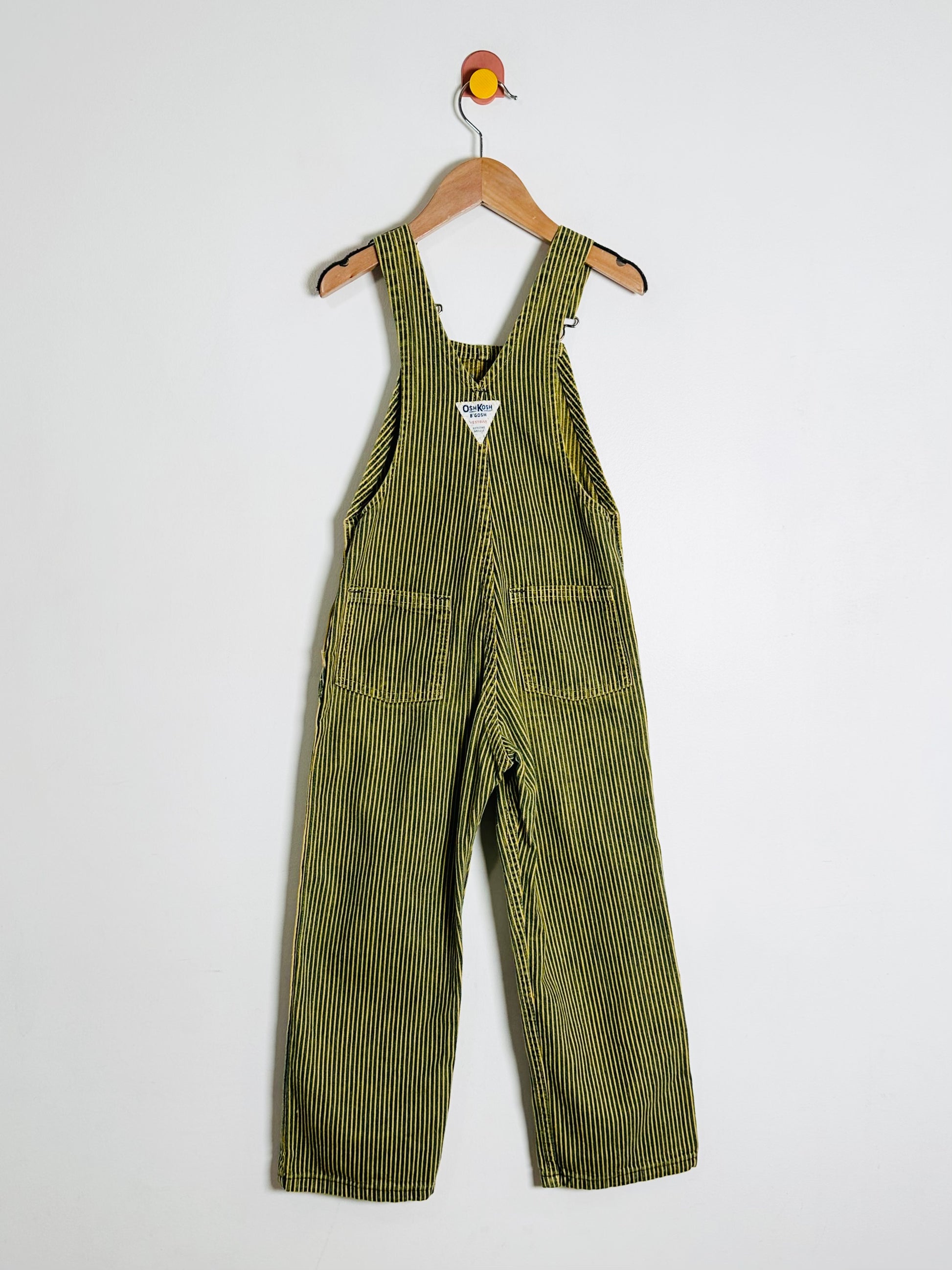 Sriped overalls hanging on a wooden hanger against a white background