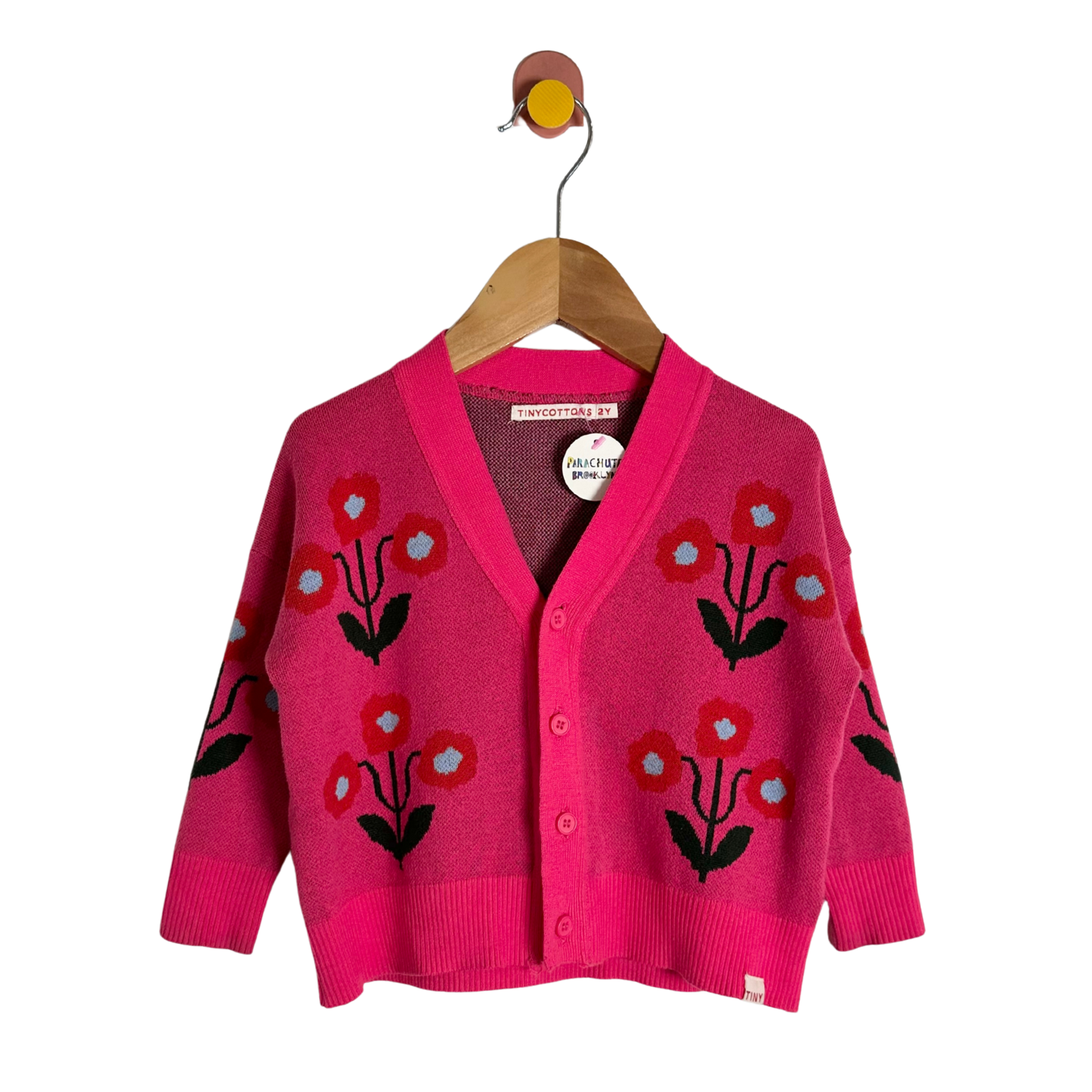 Pink cardigan with floral patterns on a wooden hanger against a white background