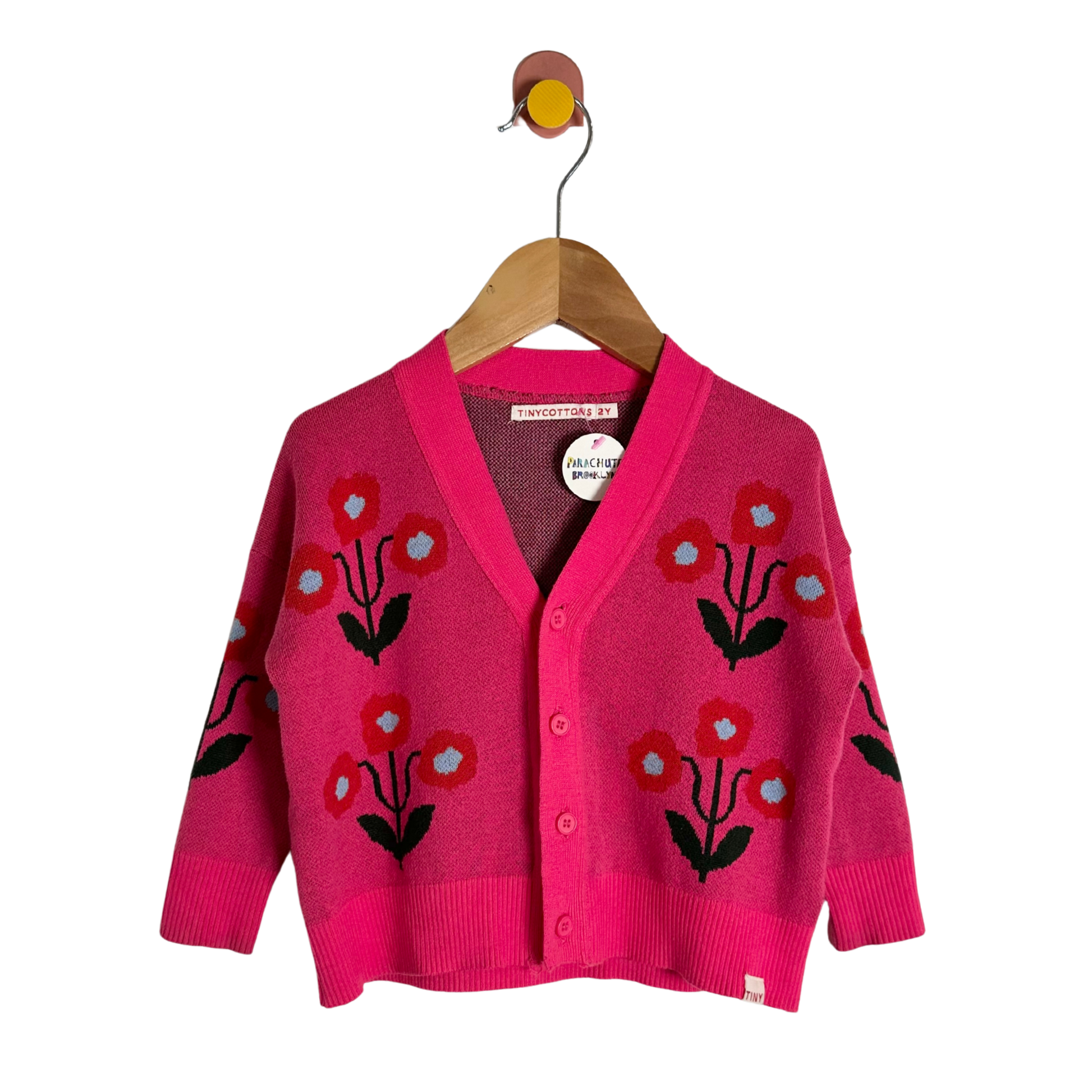 Pink cardigan with floral patterns on a wooden hanger against a white background