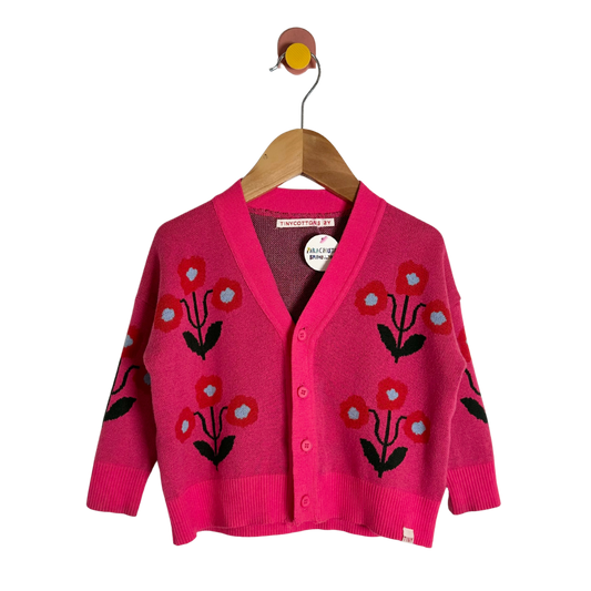 Pink cardigan with floral patterns on a wooden hanger against a white background