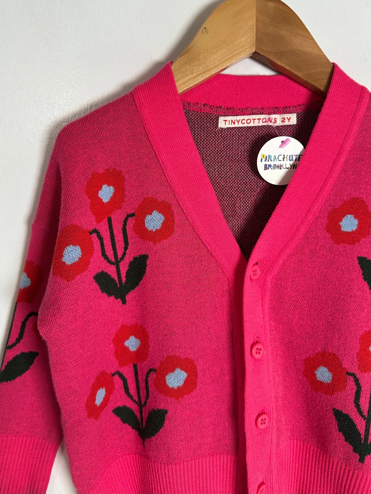 Pink cardigan with floral patterns on a wooden hanger against a white background