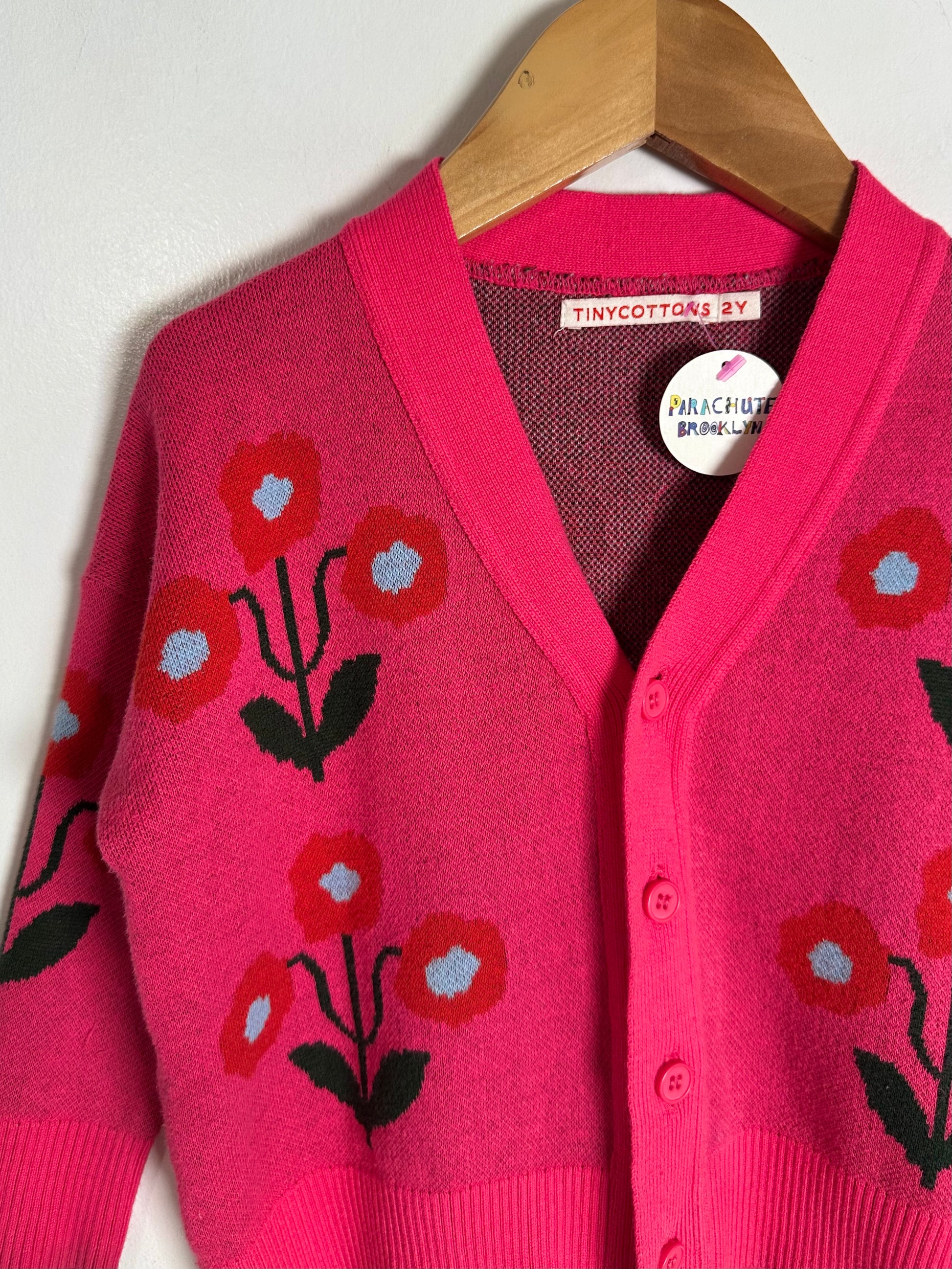 Pink cardigan with floral patterns on a wooden hanger against a white background