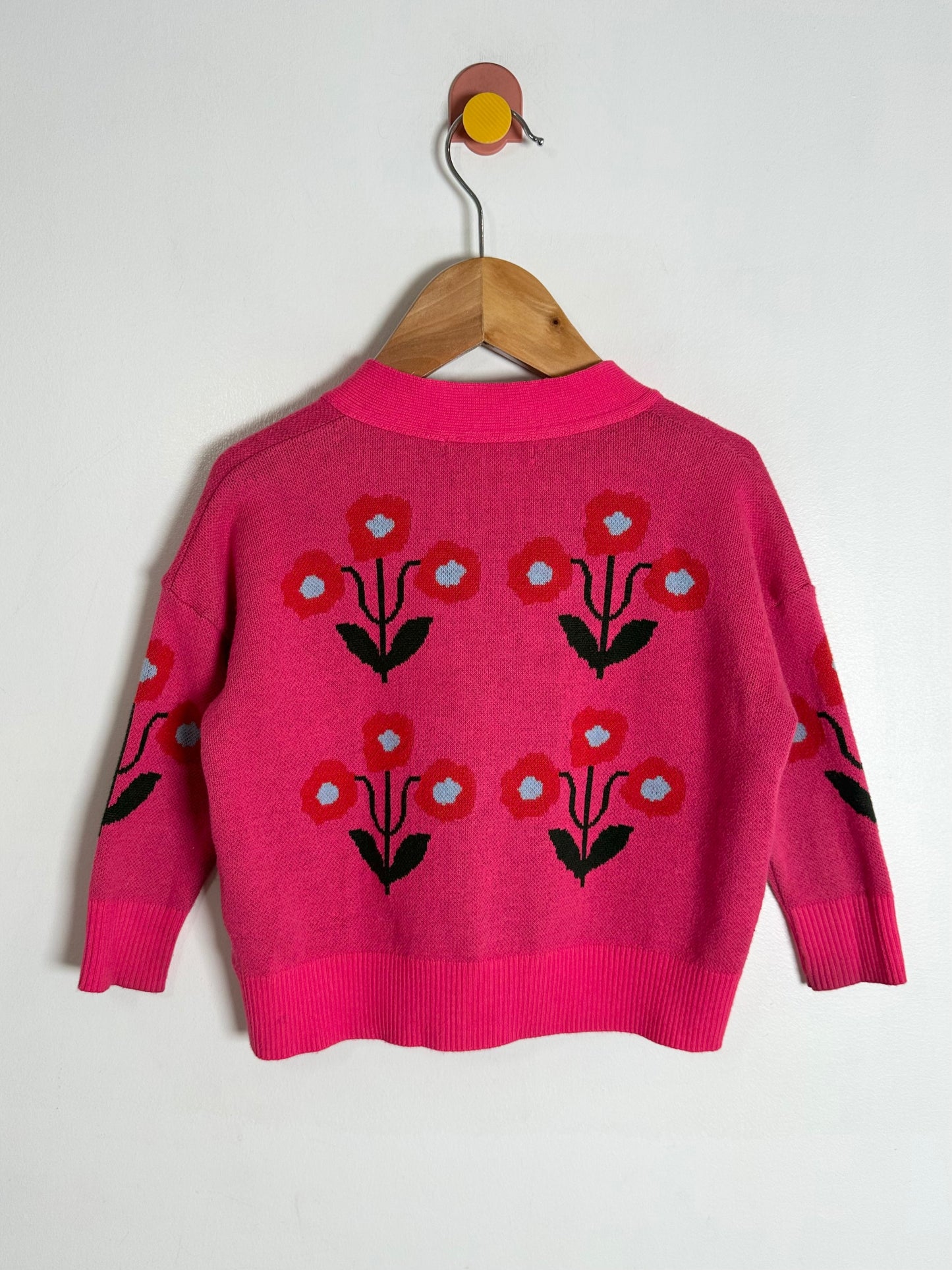Pink sweater with floral patterns on a wooden hanger against a white background