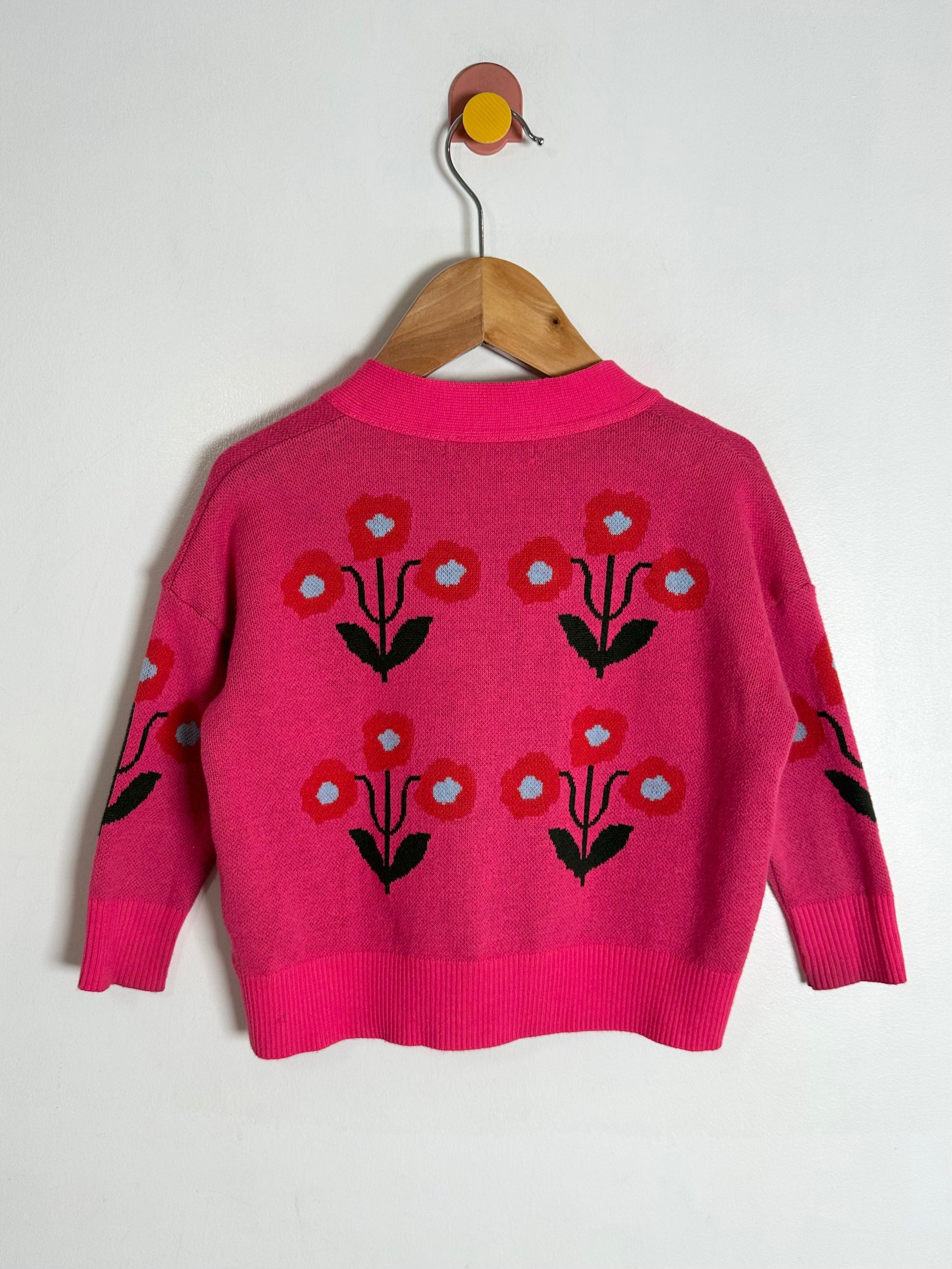 Pink sweater with floral patterns on a wooden hanger against a white background