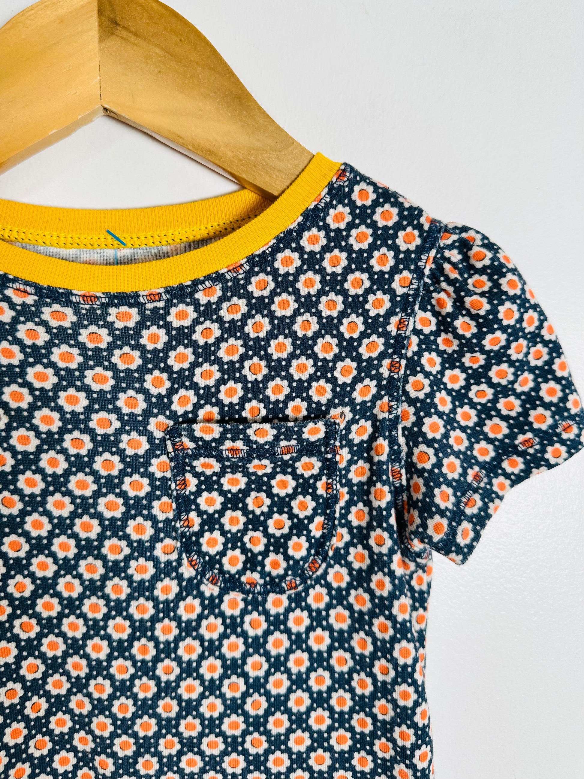 Navy blue t-shirt with small orange floral pattern on a wooden hanger against a white background