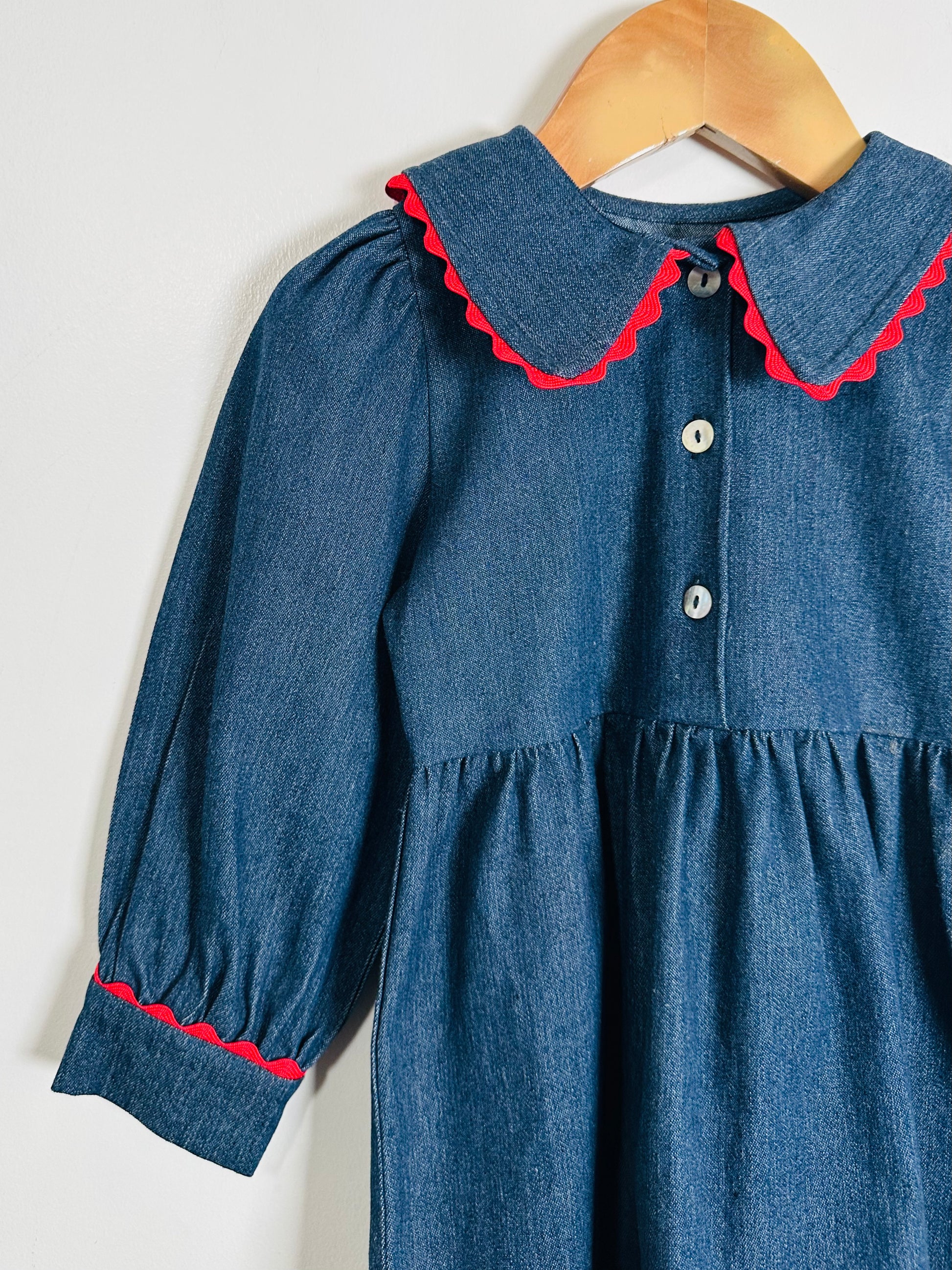 Blue dress with red trim on a wooden hanger against a white background