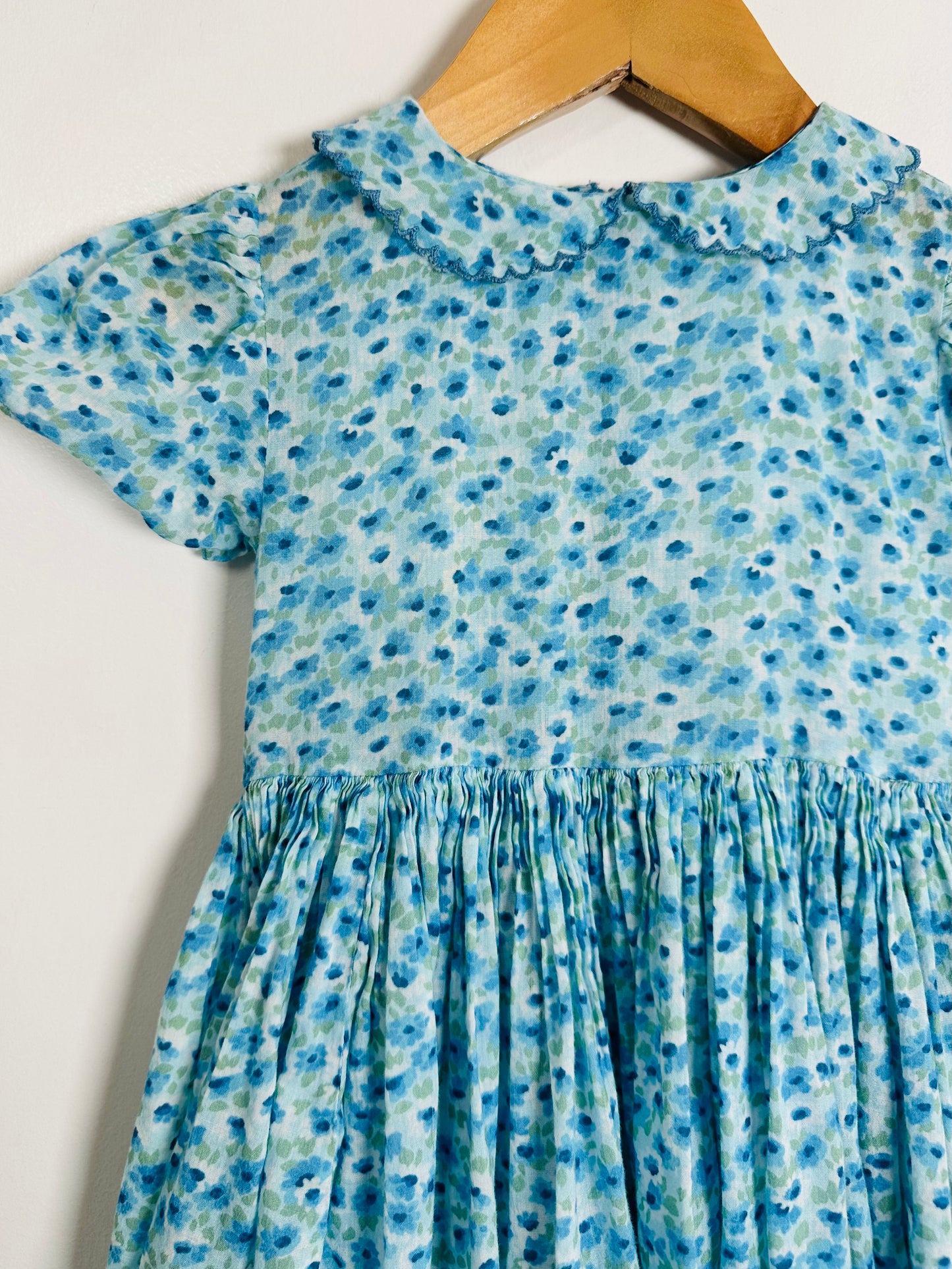 Blue floral dress on a wooden hanger against a white background