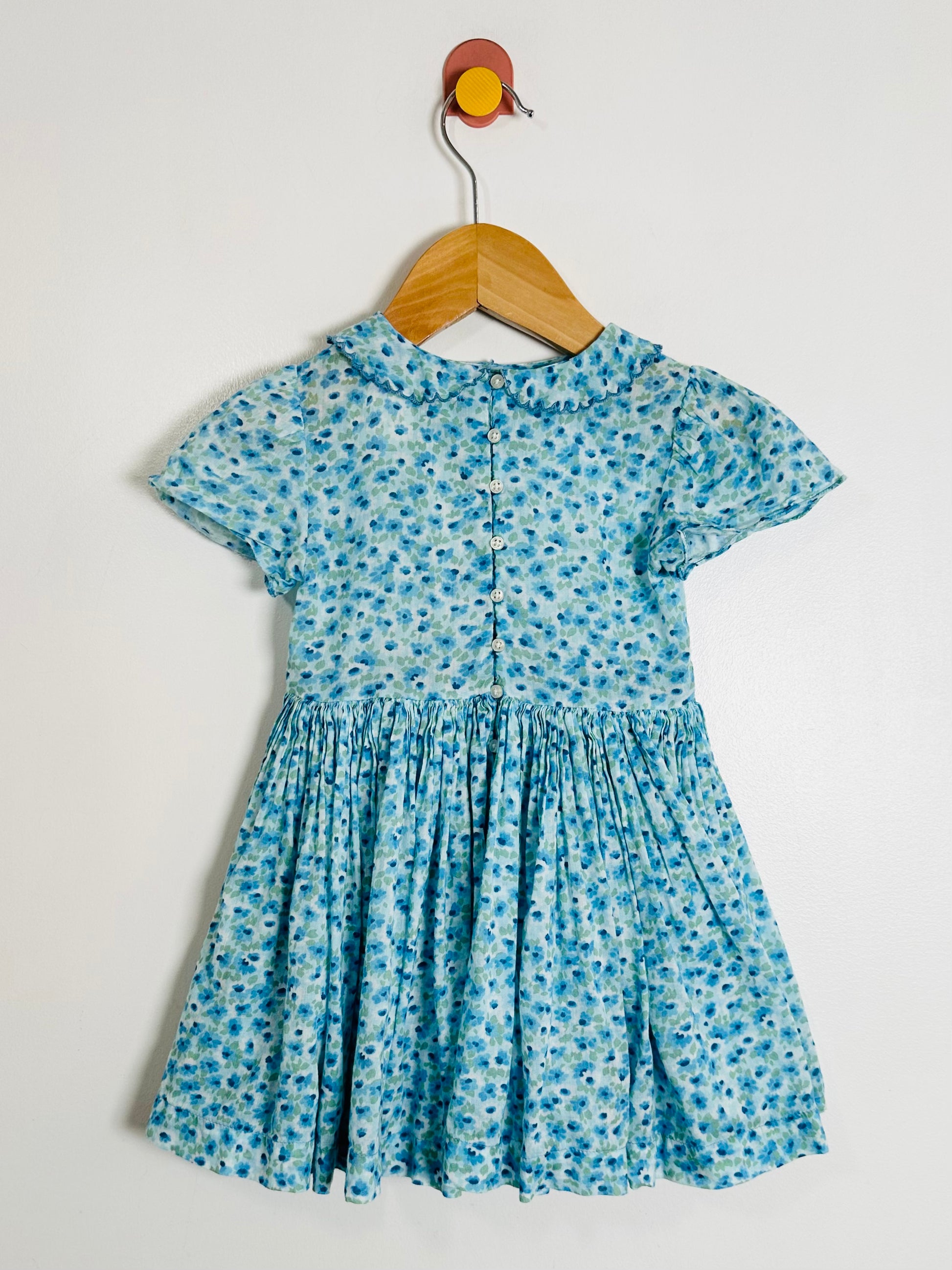 Blue floral dress on a wooden hanger against a white background