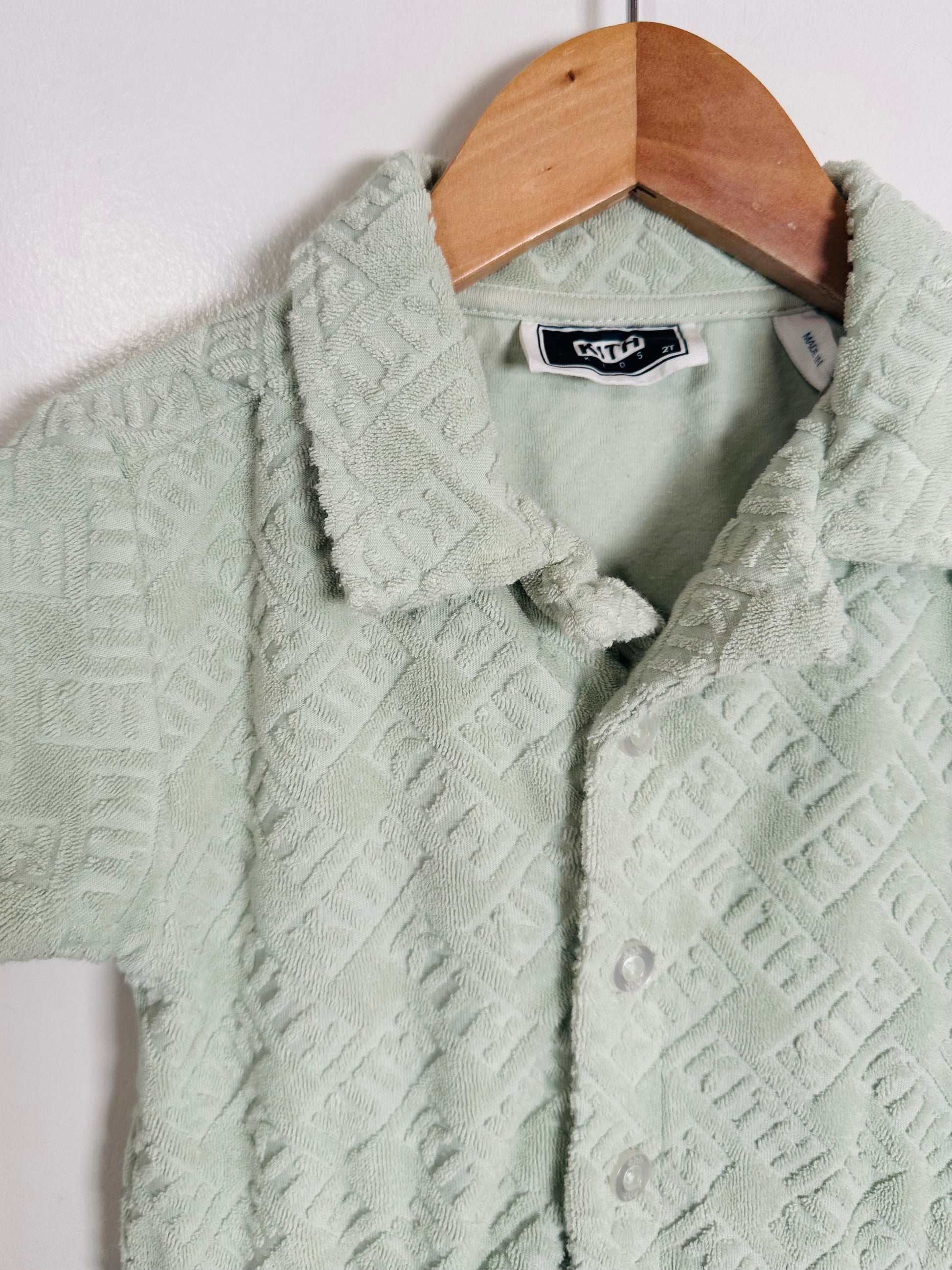 Light green textured jacket on a wooden hanger against a white background