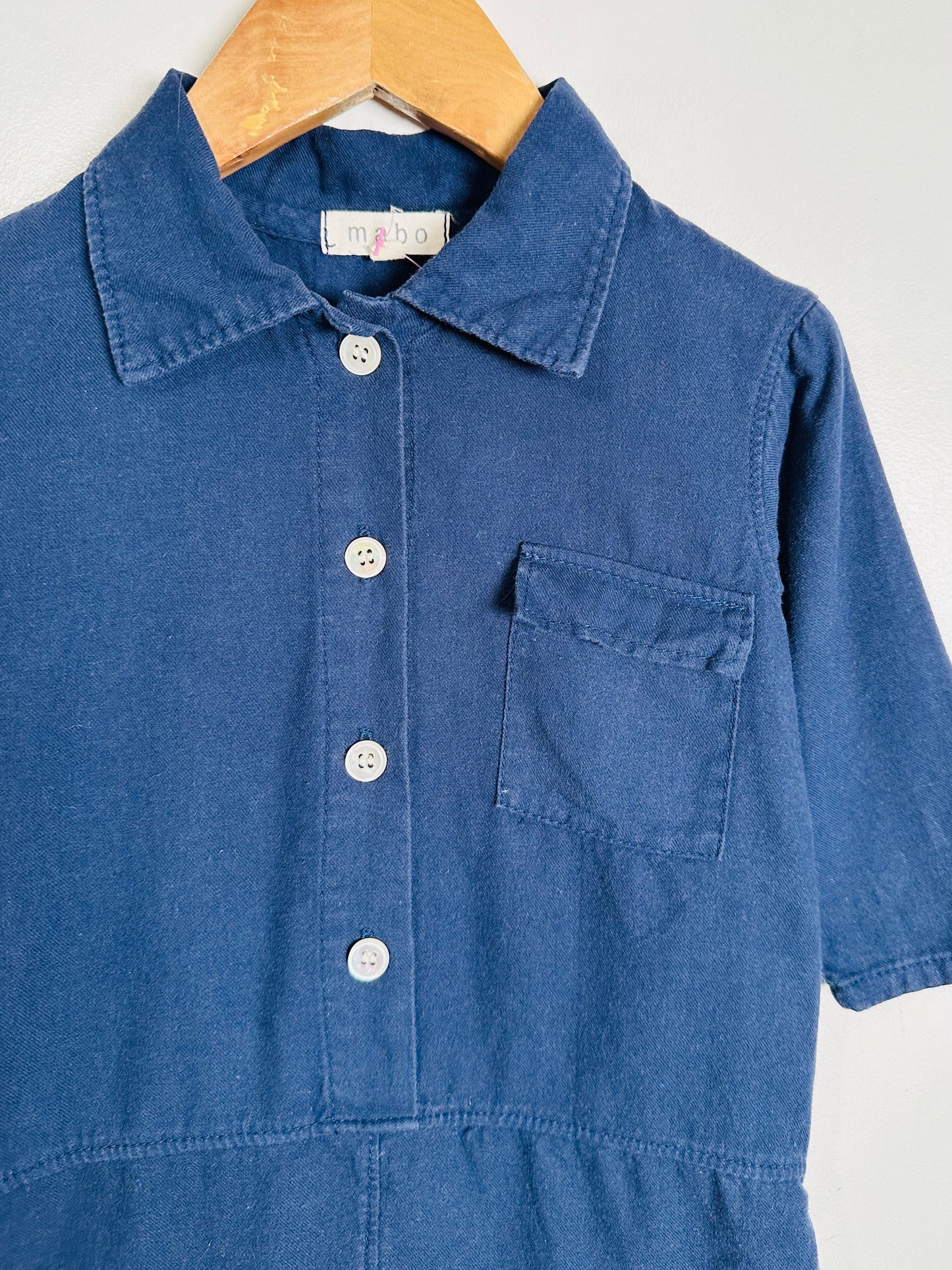 Blue romper with buttons on a hanger against a white background
