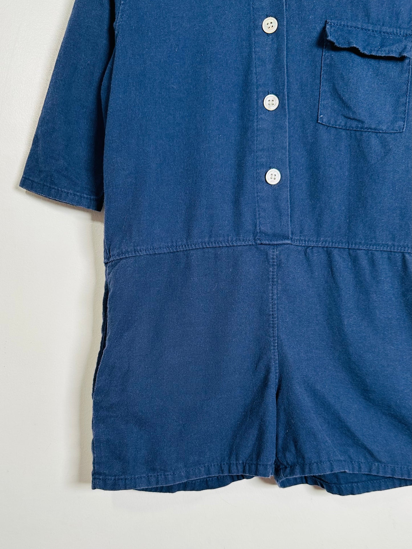 Blue romper with buttons and a pocket on a light background