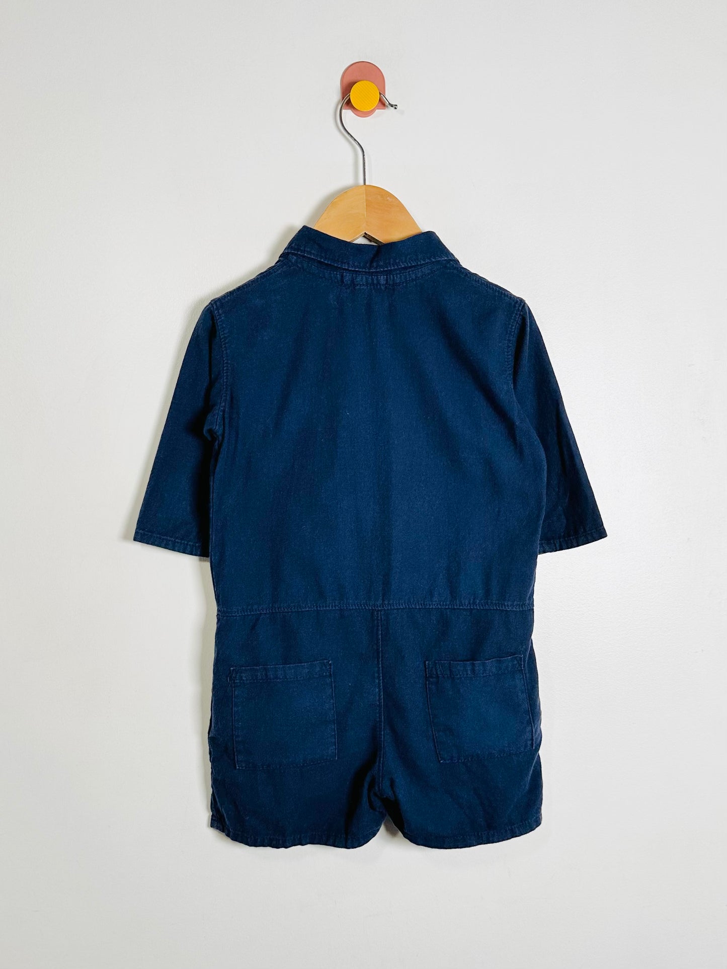 Navy blue romper on a wooden hanger against a white background