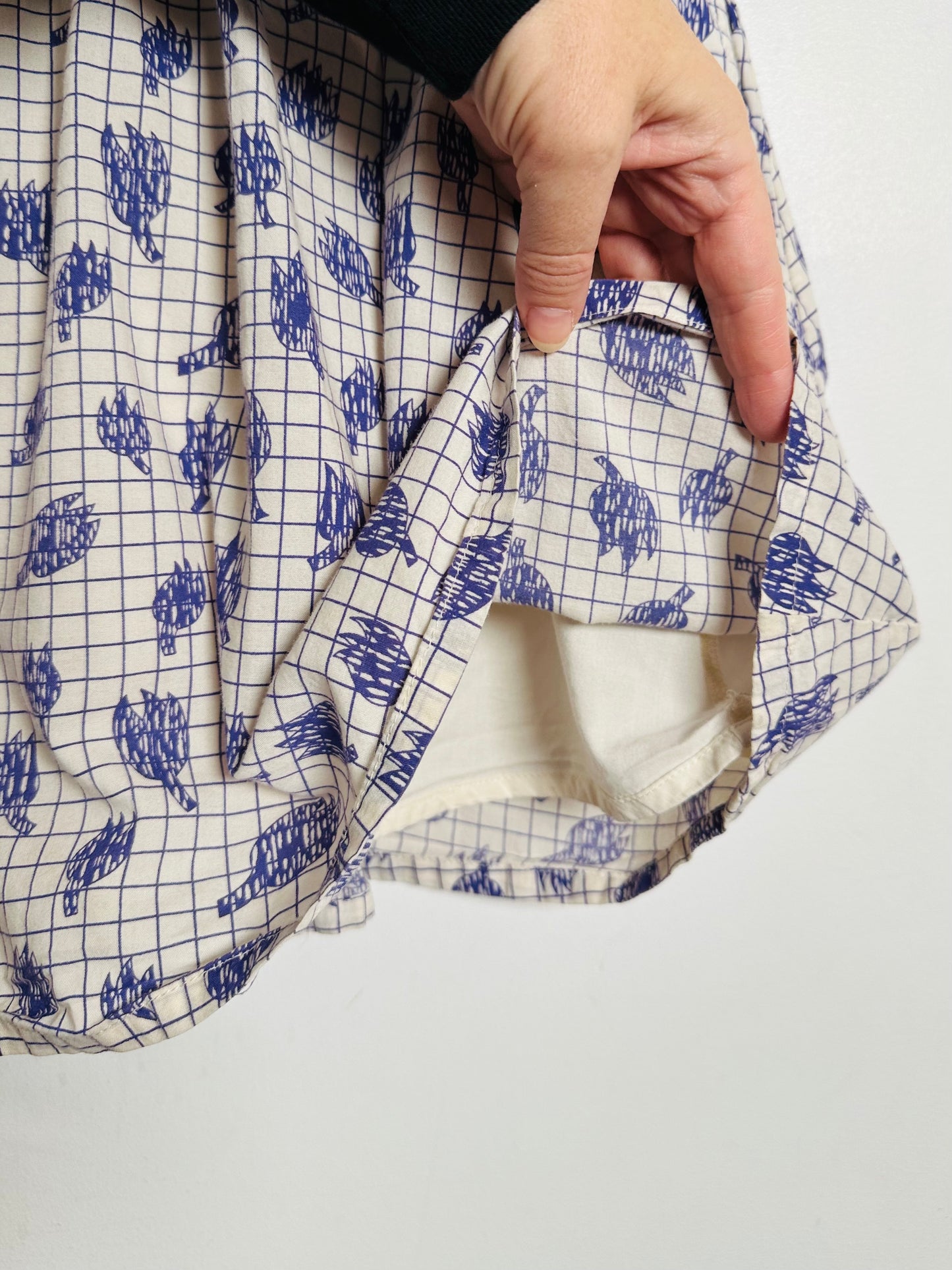 Close-up of a hand holding a patterned fabric with blue and white design on a plain background