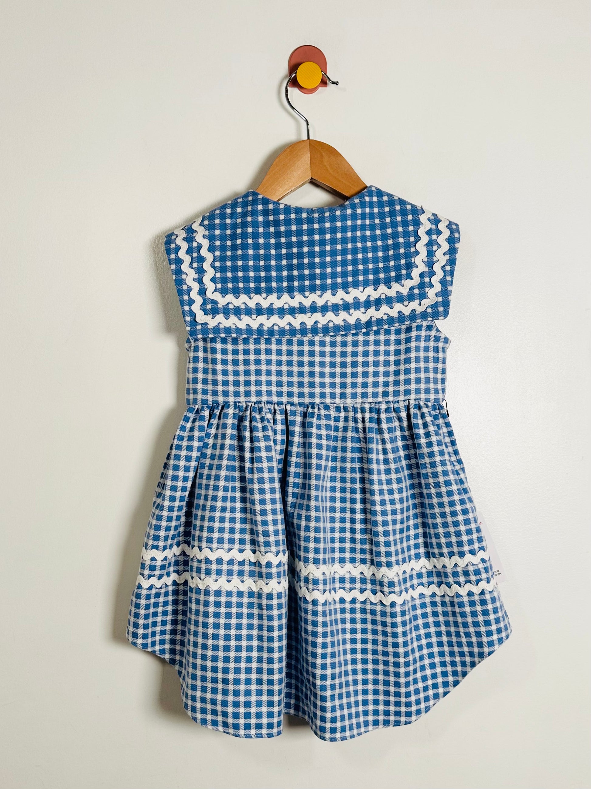 Blue checkered dress with white trim on a hanger against a light background