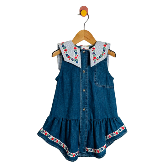 Blue denim dress with floral embroidery on a wooden hanger against a white background
