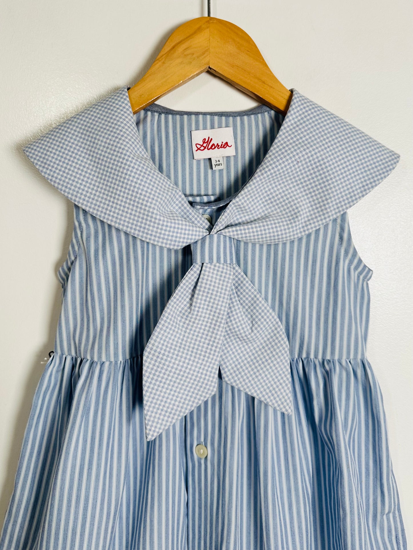 Blue and white striped dress with a large bow on a hanger against a white background