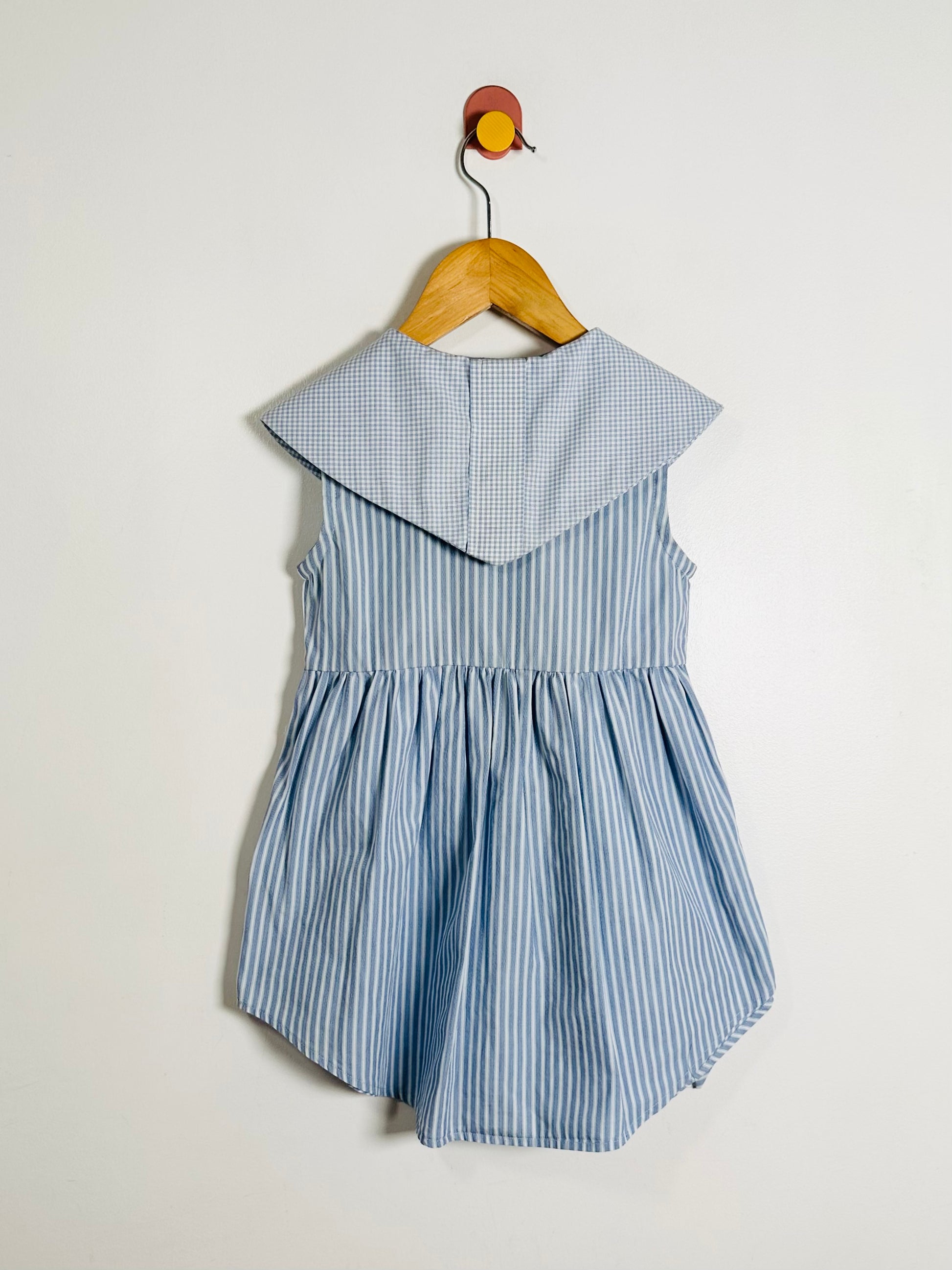 Blue striped dress on a hanger against a white background