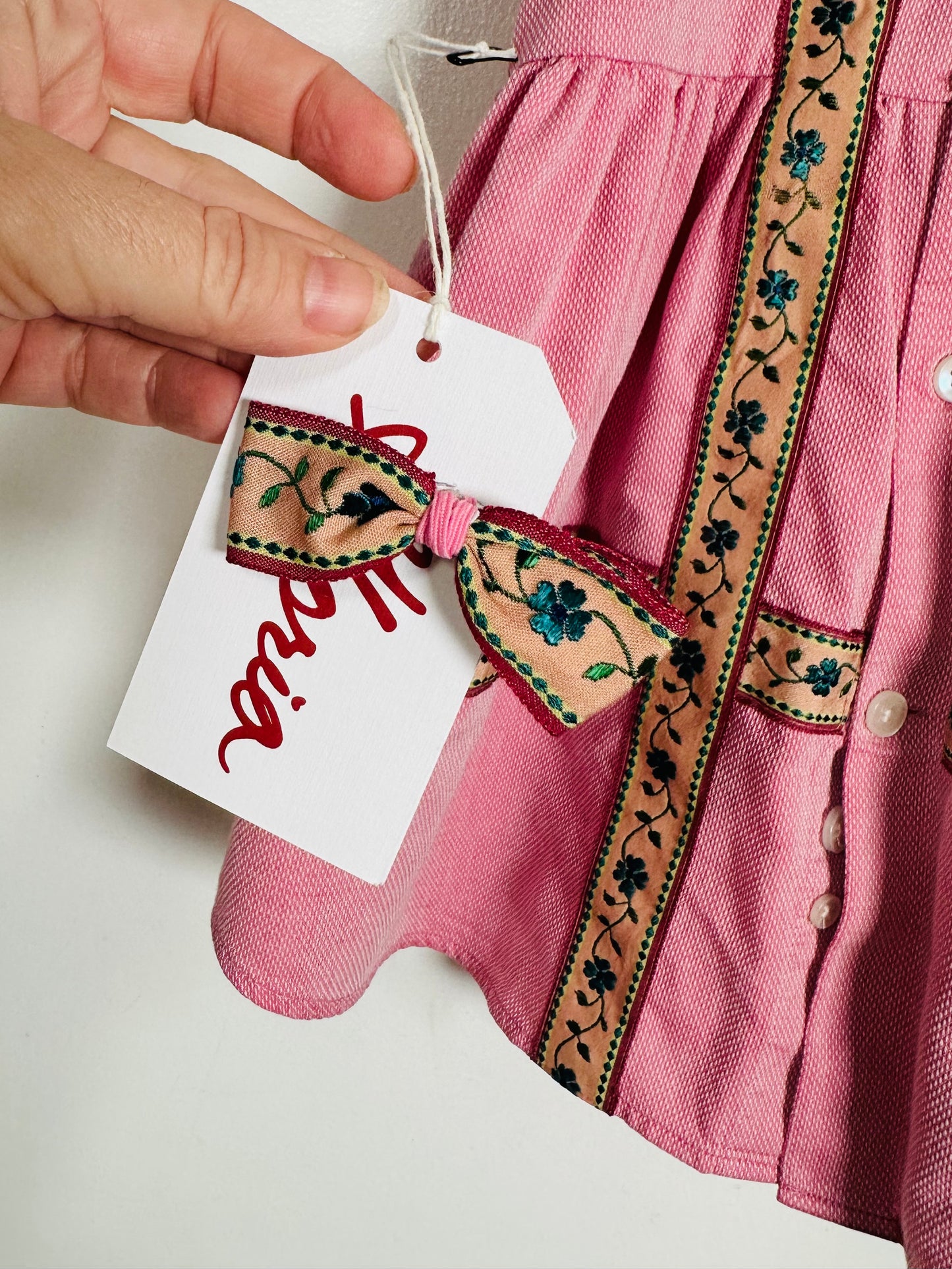 Pink dress with embroidered details and a hand holding a tag.