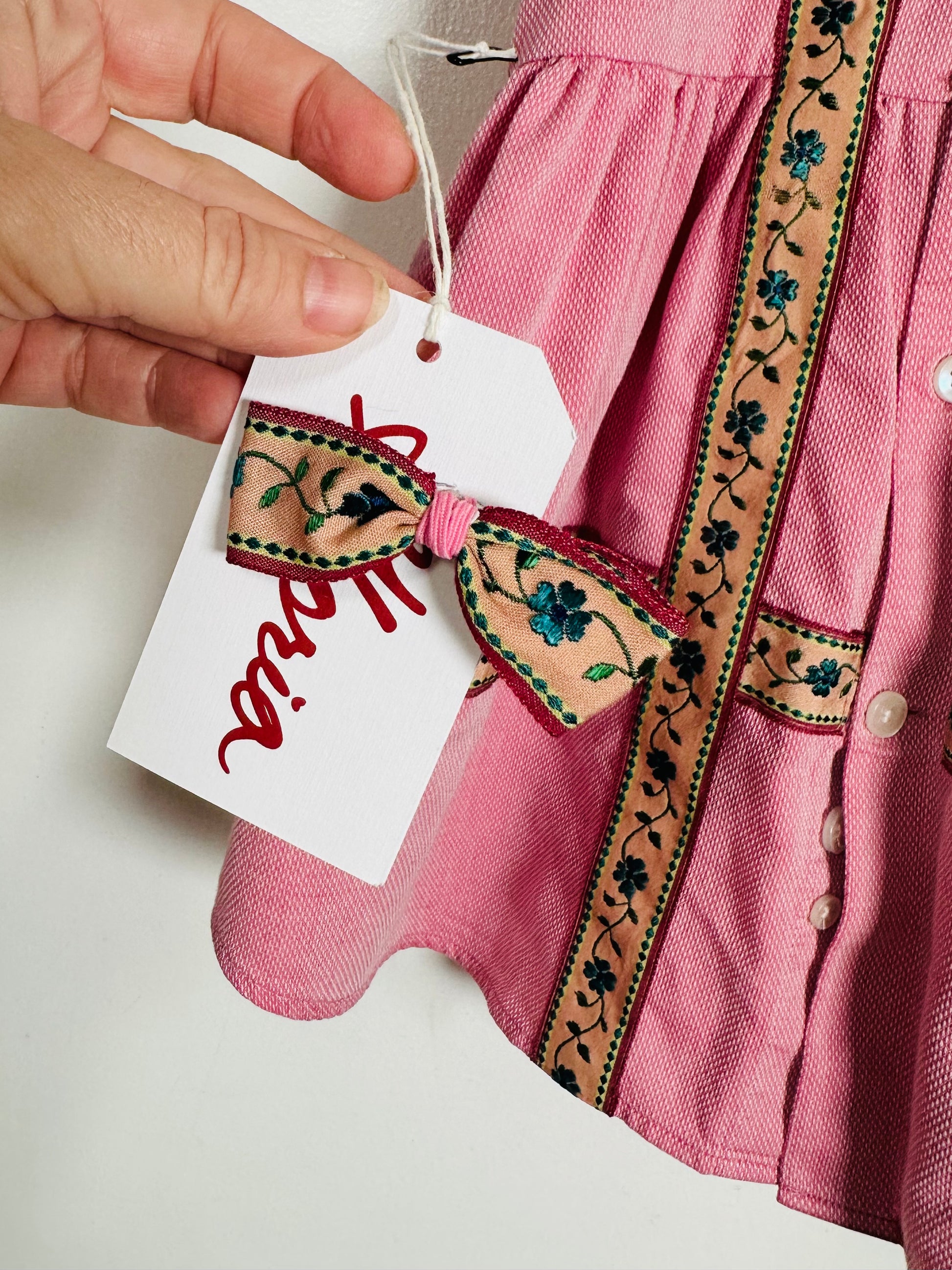 Pink dress with embroidered details and a hand holding a tag.