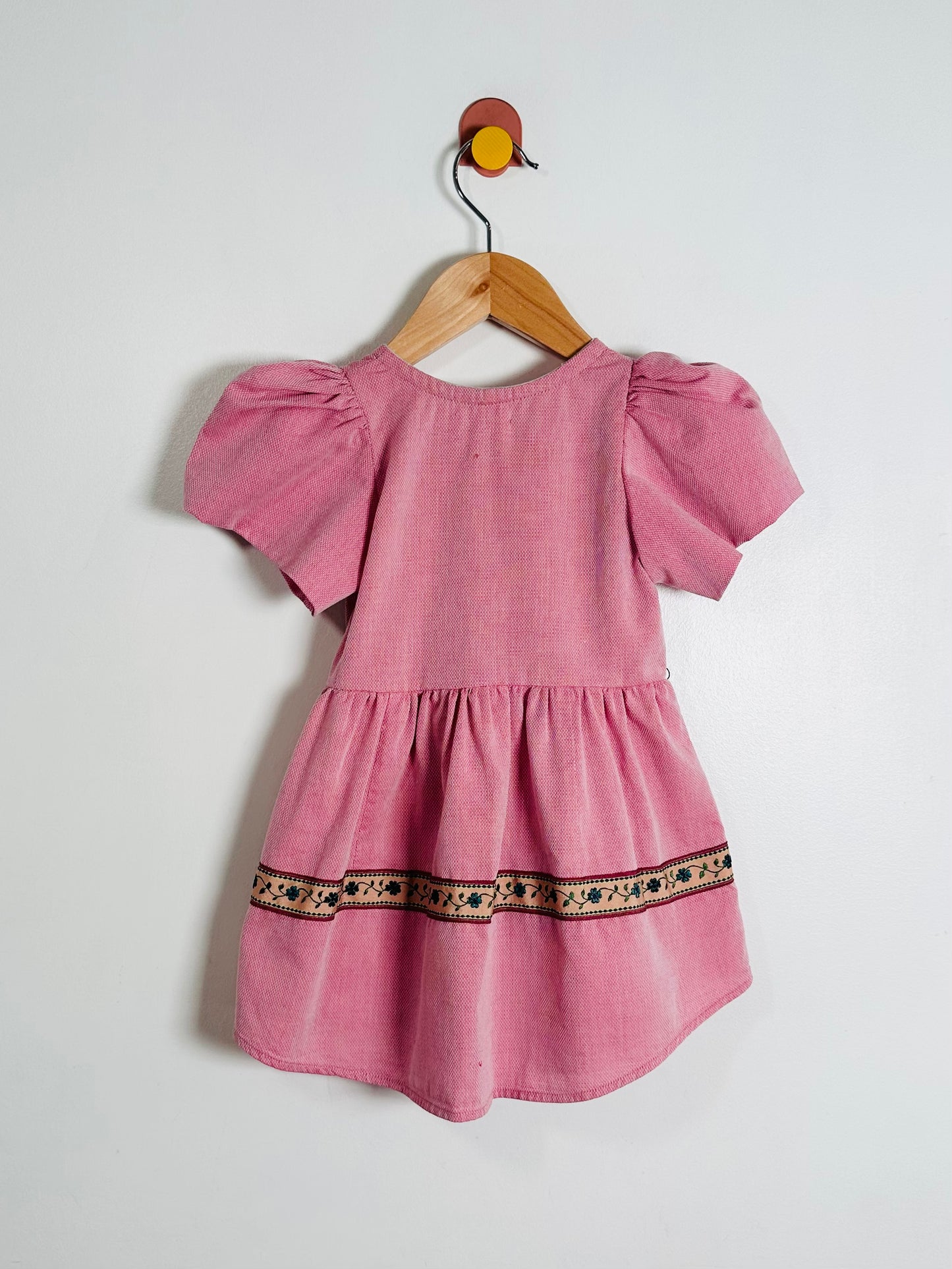 Pink dress with puff sleeves on a wooden hanger against a white background