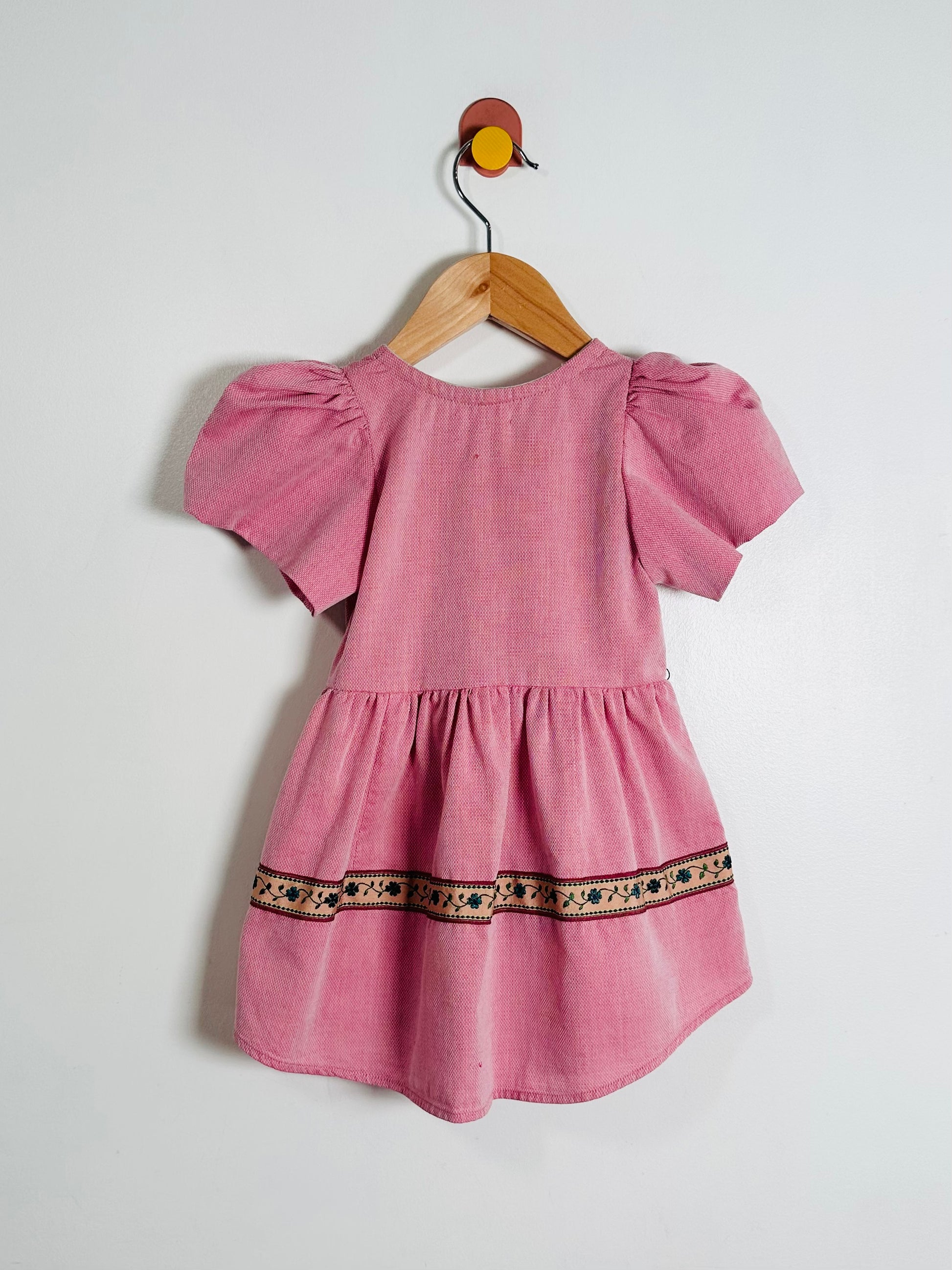 Pink dress with puff sleeves on a wooden hanger against a white background