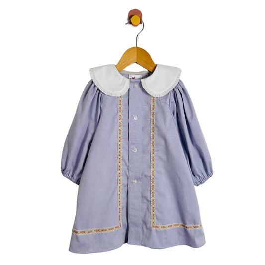 Children's dress with white collar and trim on a wooden hanger against a white background