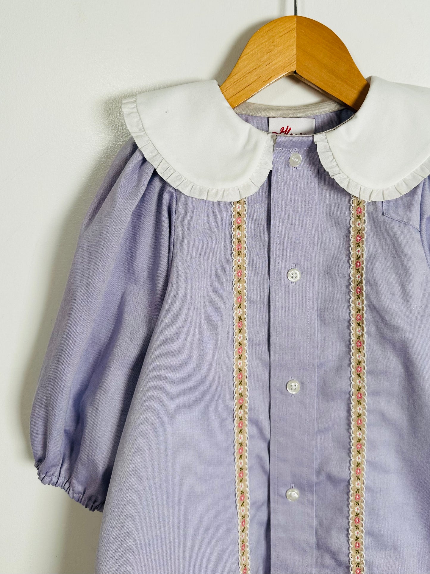 Purple dress with white collar and floral trim on a wooden hanger against a white background