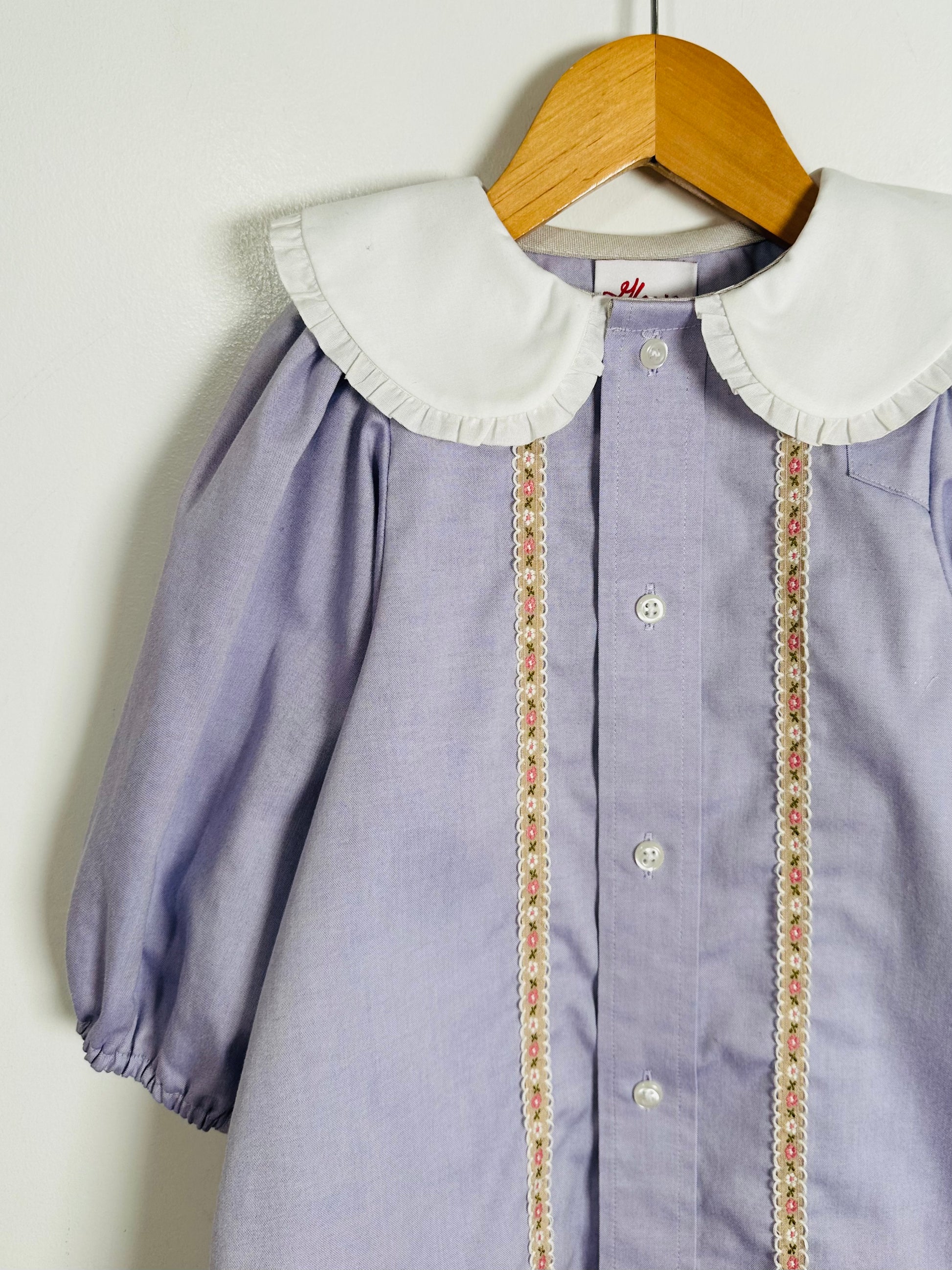 Purple dress with white collar and floral trim on a wooden hanger against a white background