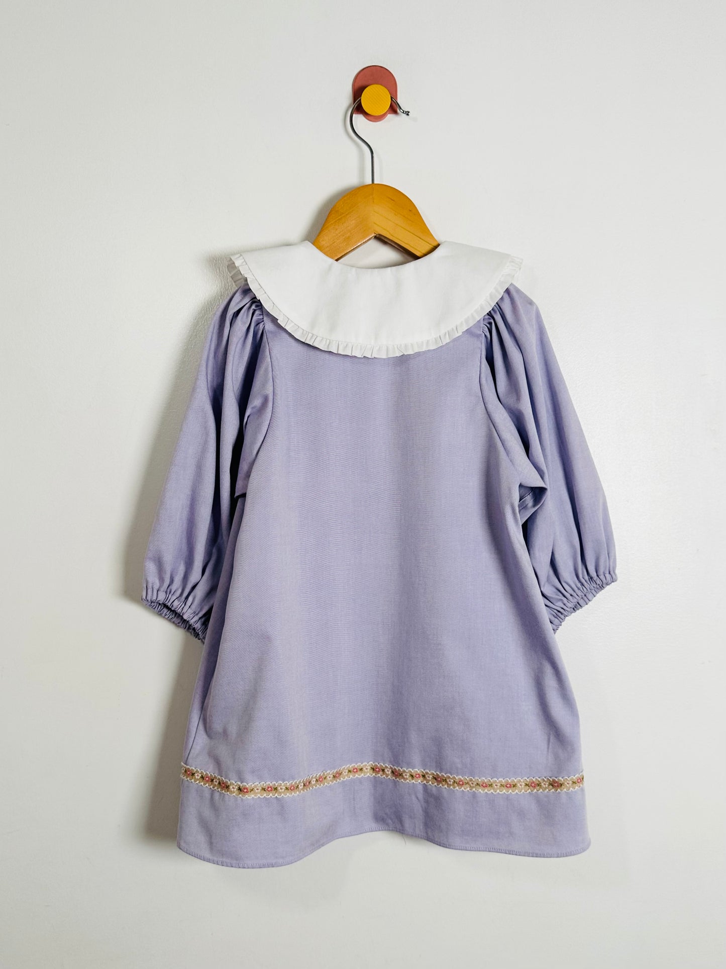 Lavender dress with white collar on a wooden hanger against a light gray background
