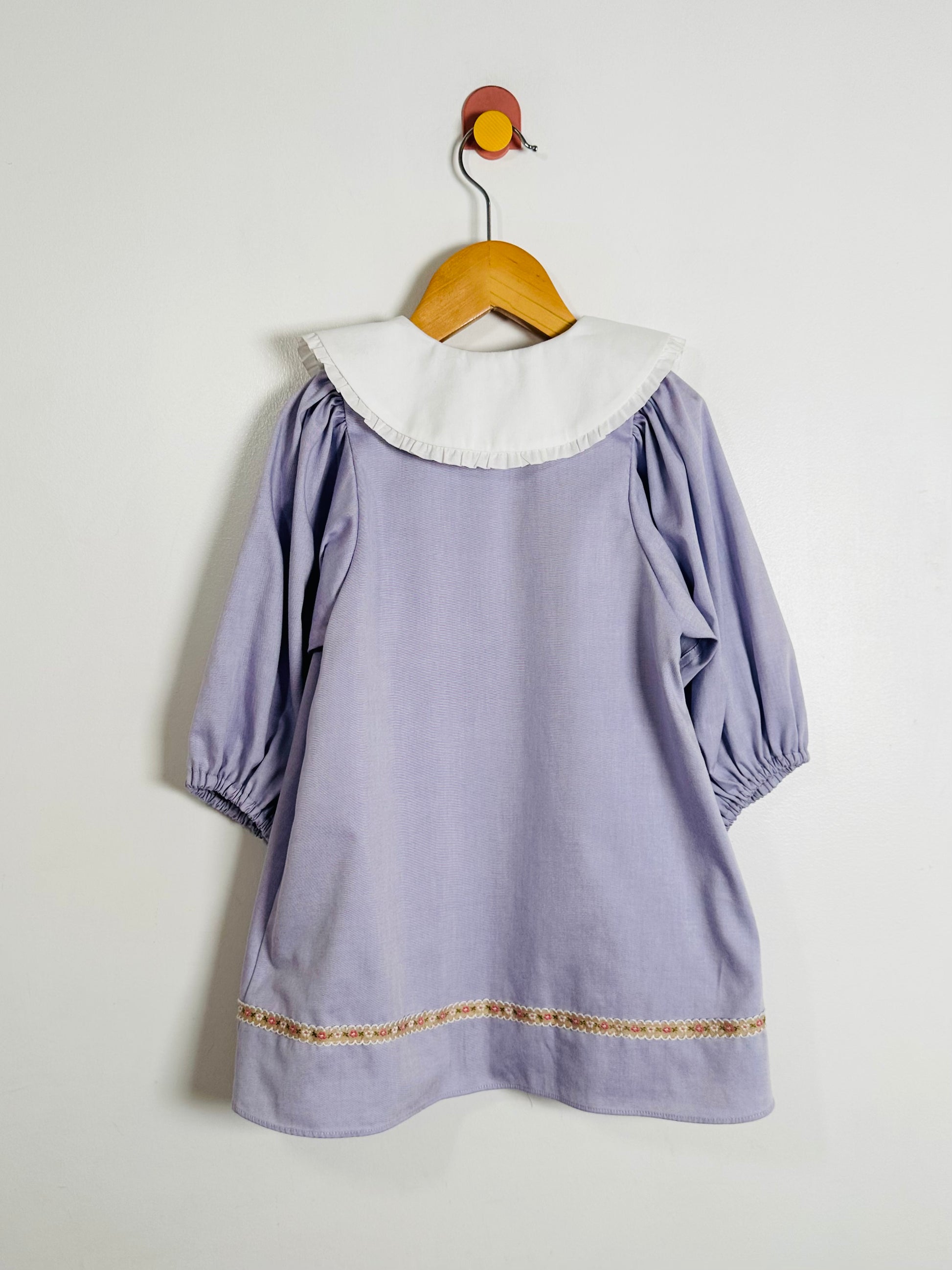 Lavender dress with white collar on a wooden hanger against a light gray background