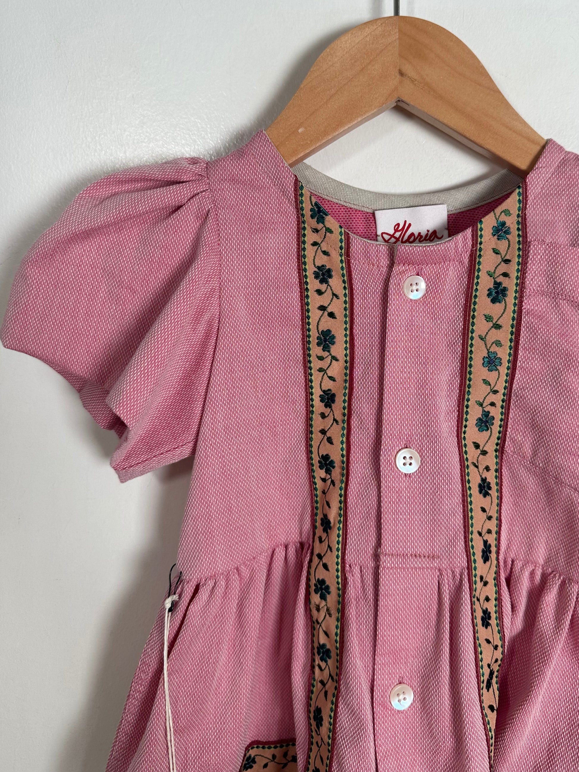 Pink dress with embroidery on a wooden hanger against a white background