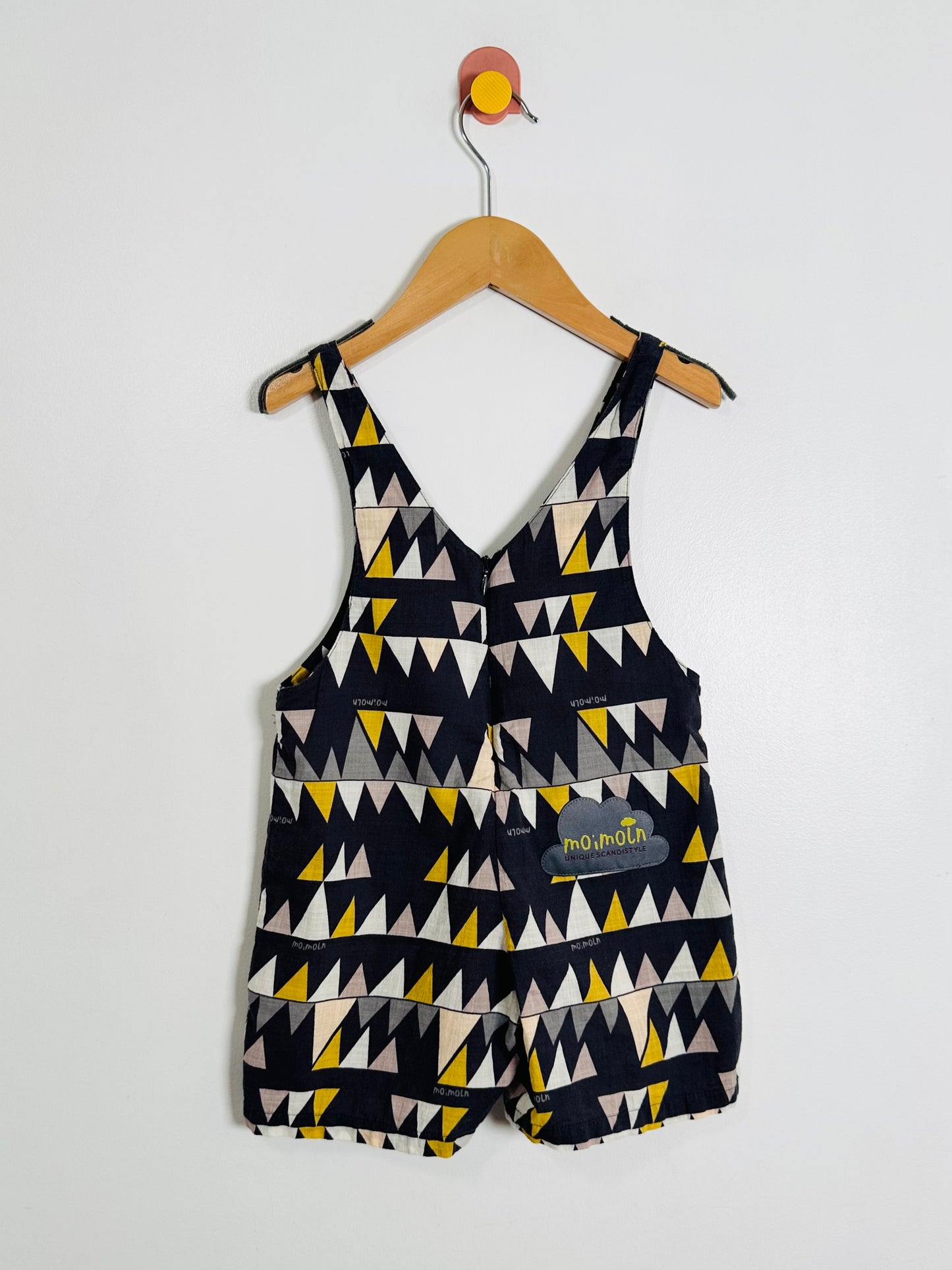 Children's patterned overalls on a hanger against a white background