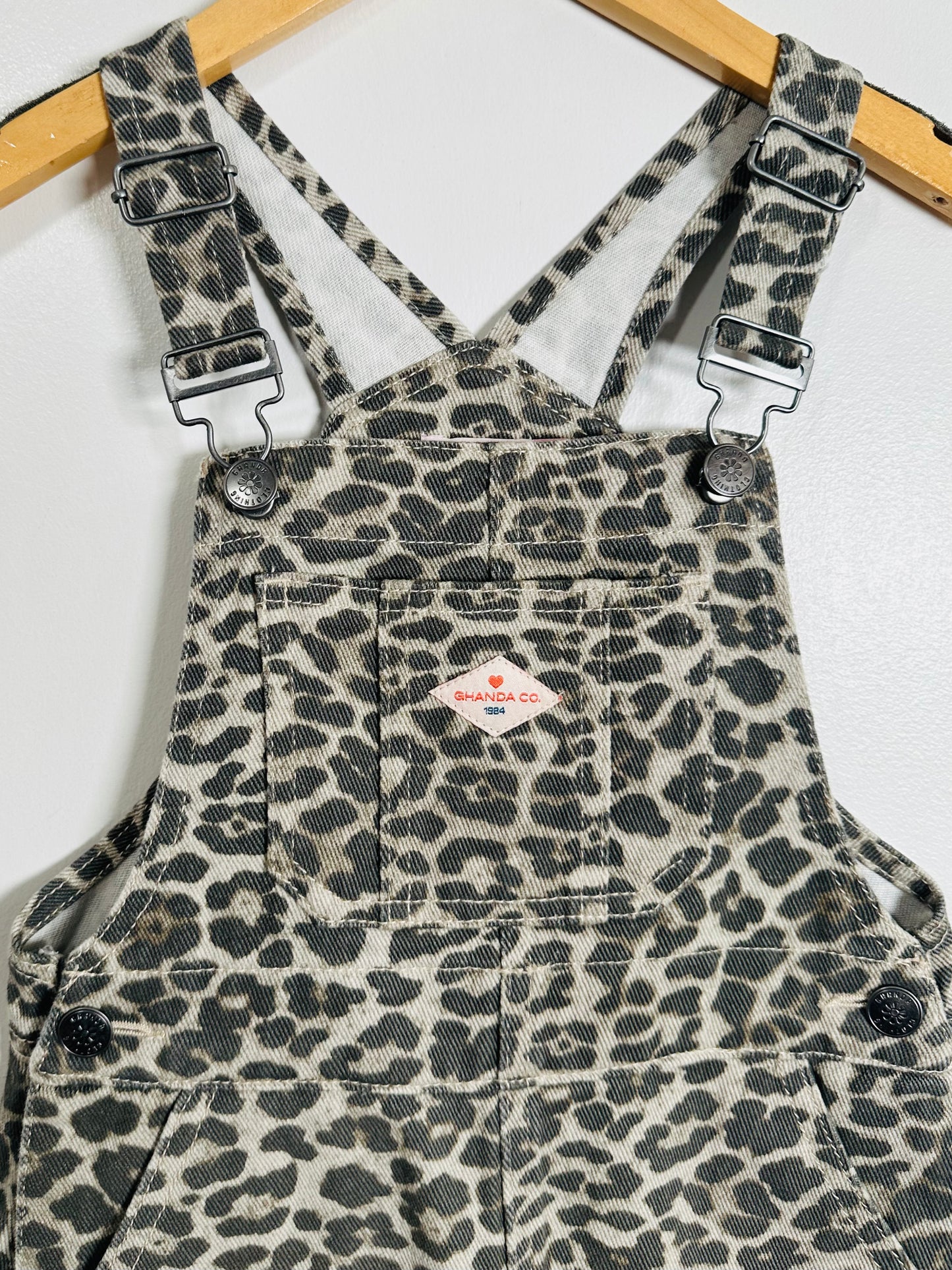 Leopard print overalls on a hanger against a white background