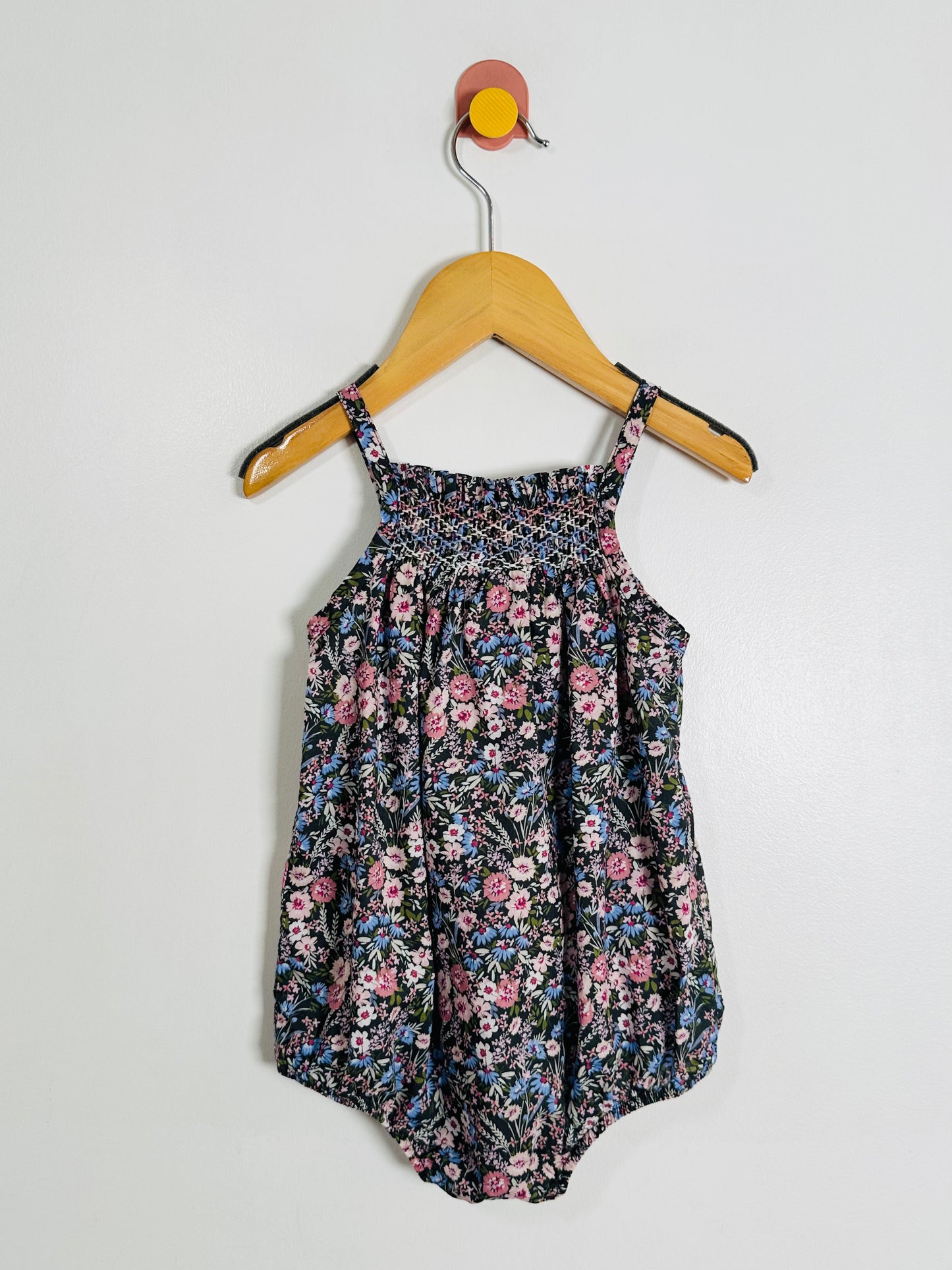 Floral-patterned romper on a hanger against a white background