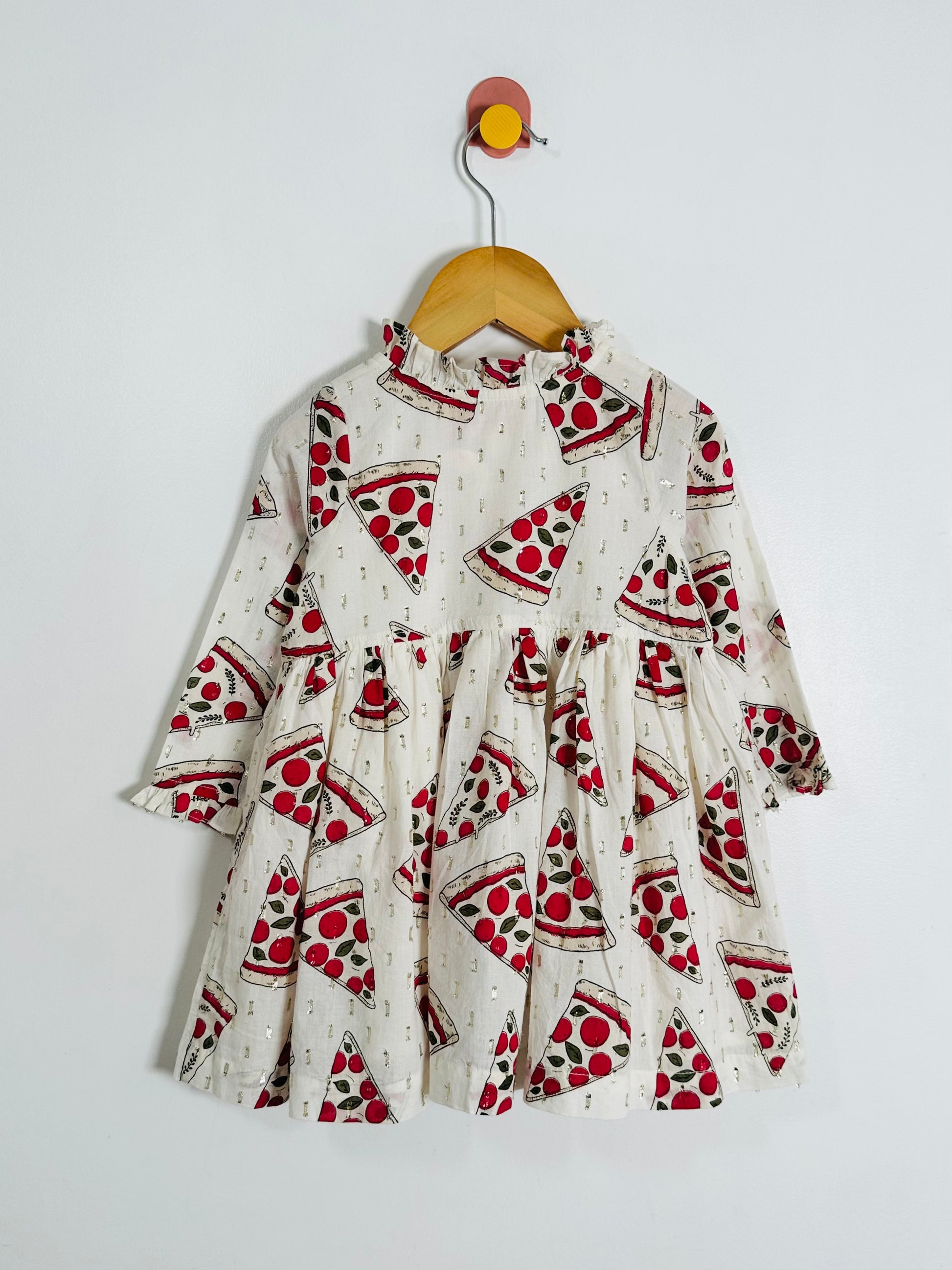 Children's dress with pizza print on a hanger against a white background