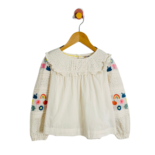 White blouse with rainbow and flower designs on a wooden hanger against a white background